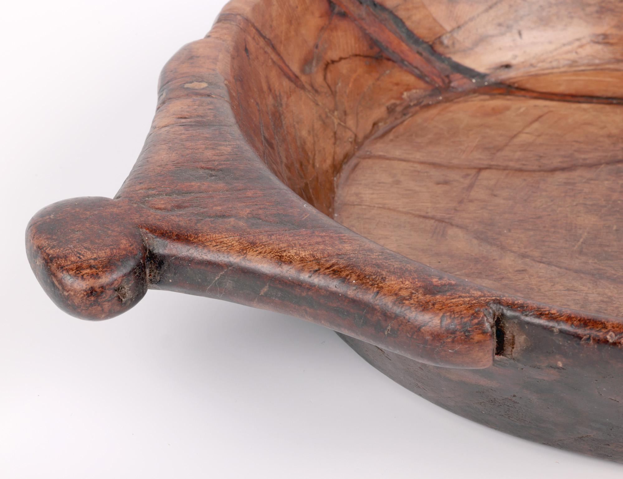 A stylish vintage African hand-carved twin handled wooden bowl dating from the early to mid-20th century. The bowl is made from a single piece of native wood and is of wide shallow round shape with shaped flat handles carved to two sides. The bowl