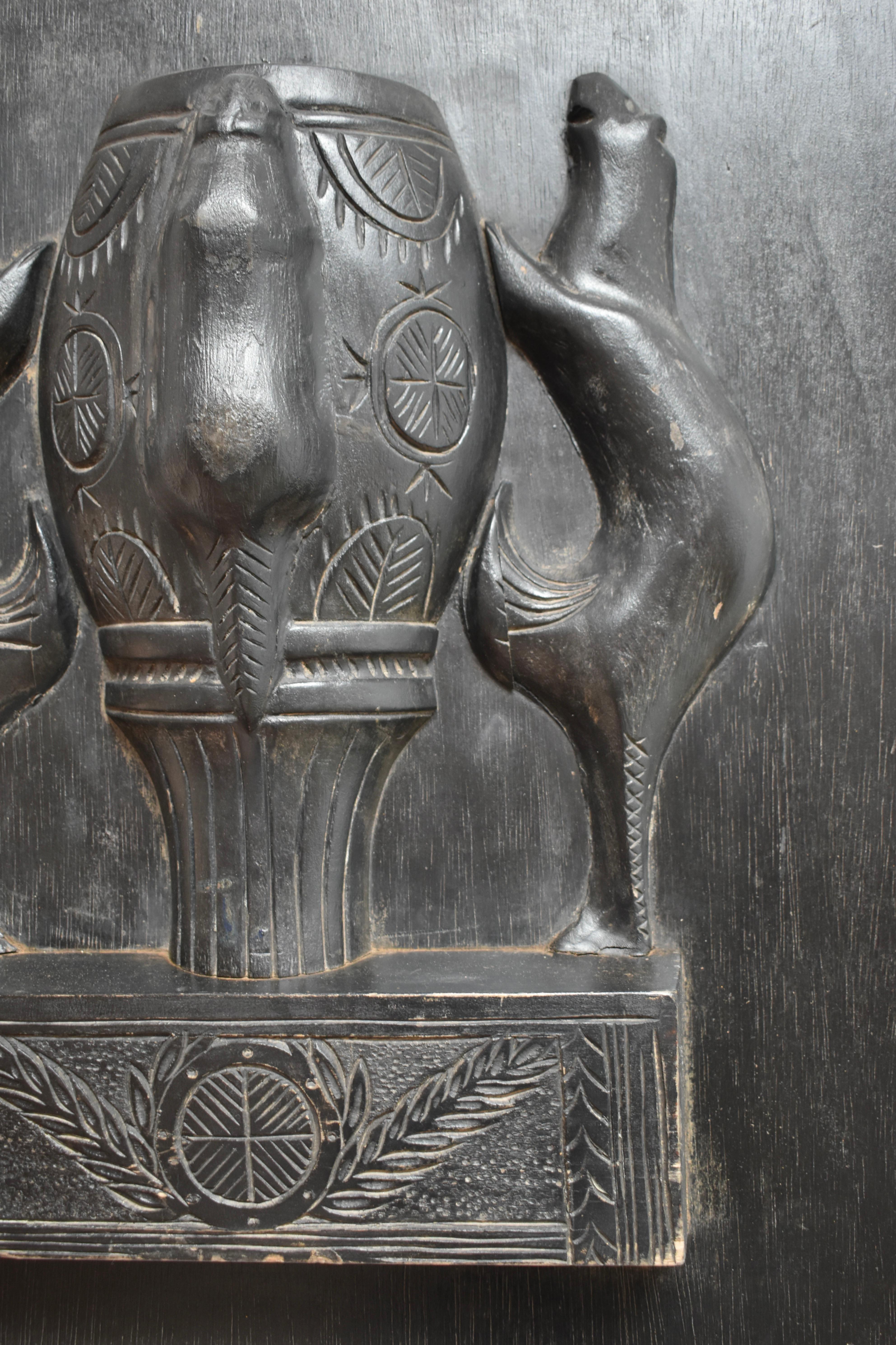 Elemento decorativo murale africanista in legno ebanizzato a basso rilievo con motivo di animali intorno a un vaso centrale. Francia, anni '60.