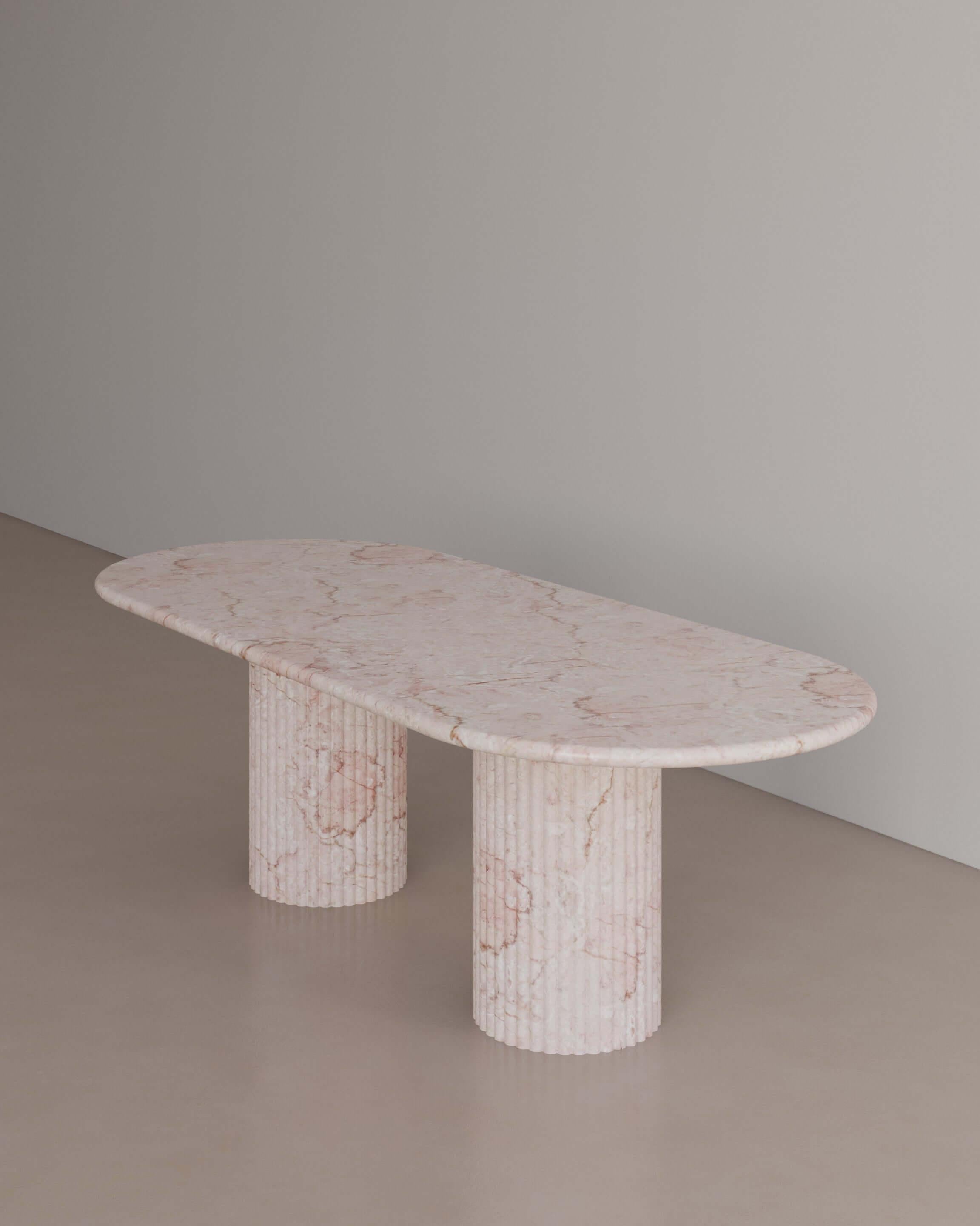 The Essentialist brings you The Antica Dining Table II in Afshar Pink Marble. An oval table top resolved by smooth bullnose edges rests on two supporting pillars. Architectural form is refined by artistic expression echoing Roman culture. This