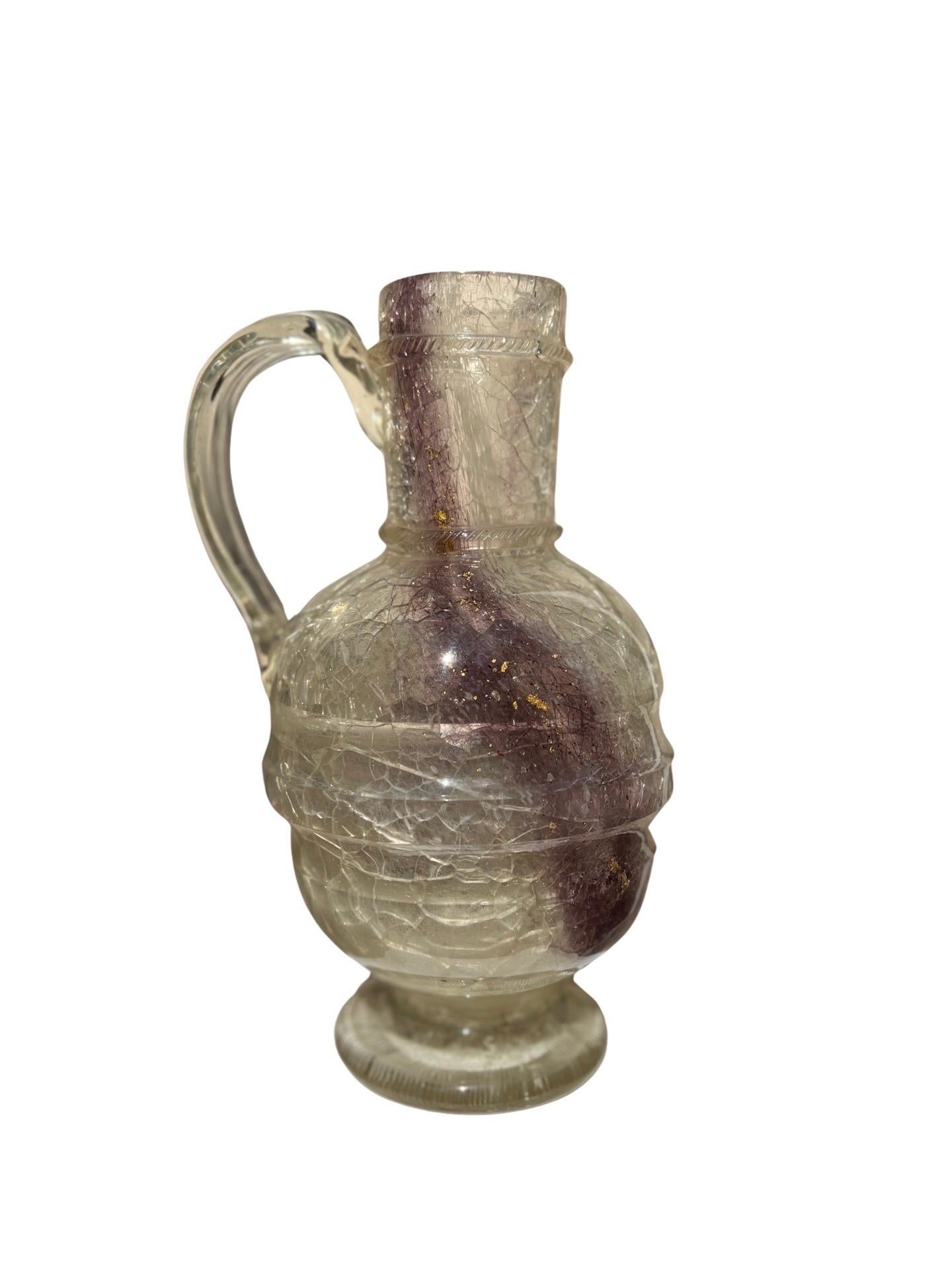 Likely European, 19th century or earlier.

This pitcher is incredibly unique and unusual. The interior has a cracked rock crystal surface, purple striations and gold flecking which appears to be encased with a glass surface and applied handle. 
A