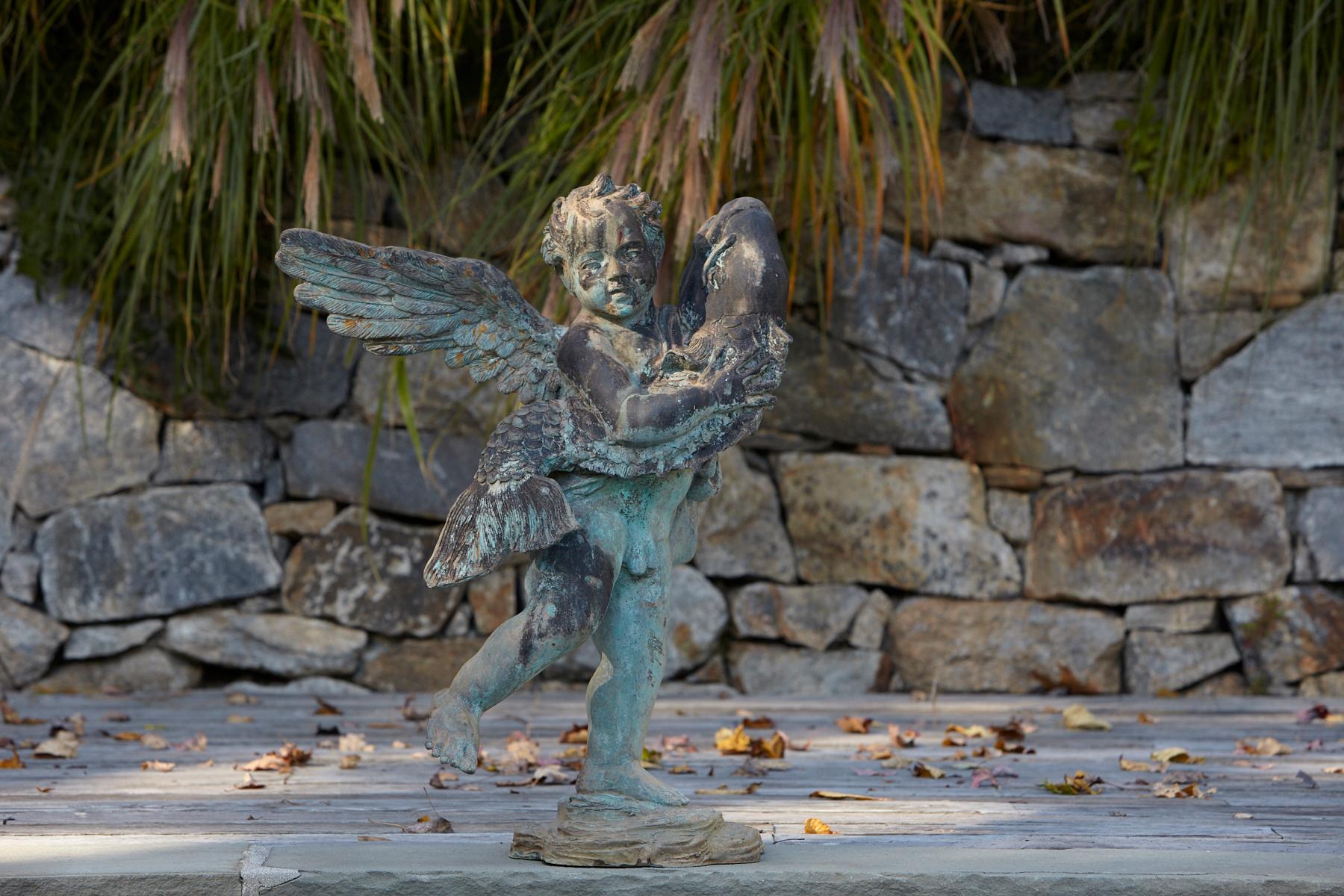 After Andrea del Verrocchio, a beautifully detailed bronze water garden/fountain statue of a cherub with large wings holding a fish in his arms, circa 1940s. The statue has a wonderful, lovely green patina. The statue is piped.
   