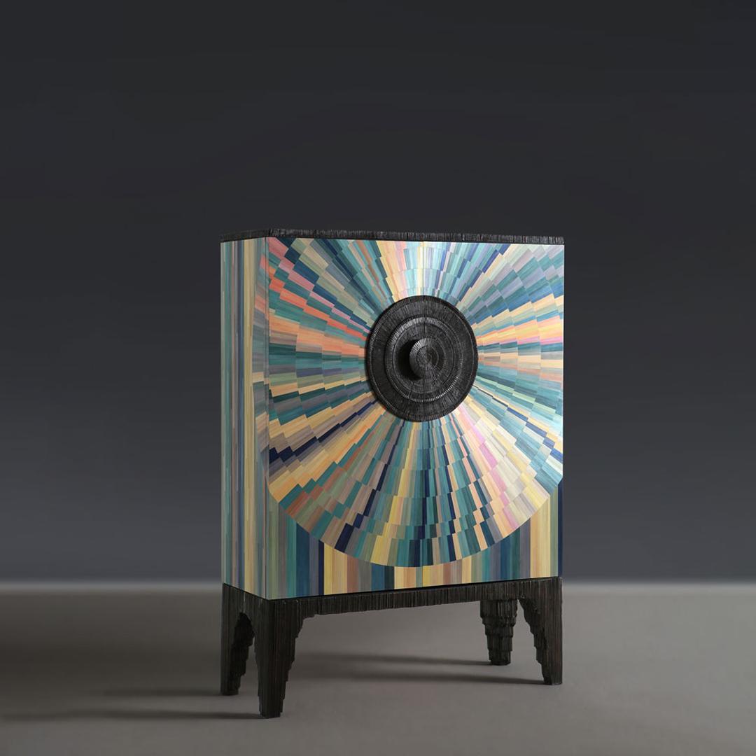 A dresser cabinet covered in a whirl of hand-dyed straw marquetry rings that ripple out from sculpted handles. Bronze is also used to cast the powerful top and base. The interior is finished in succulent dark Wenge veneer that has been lacquered and