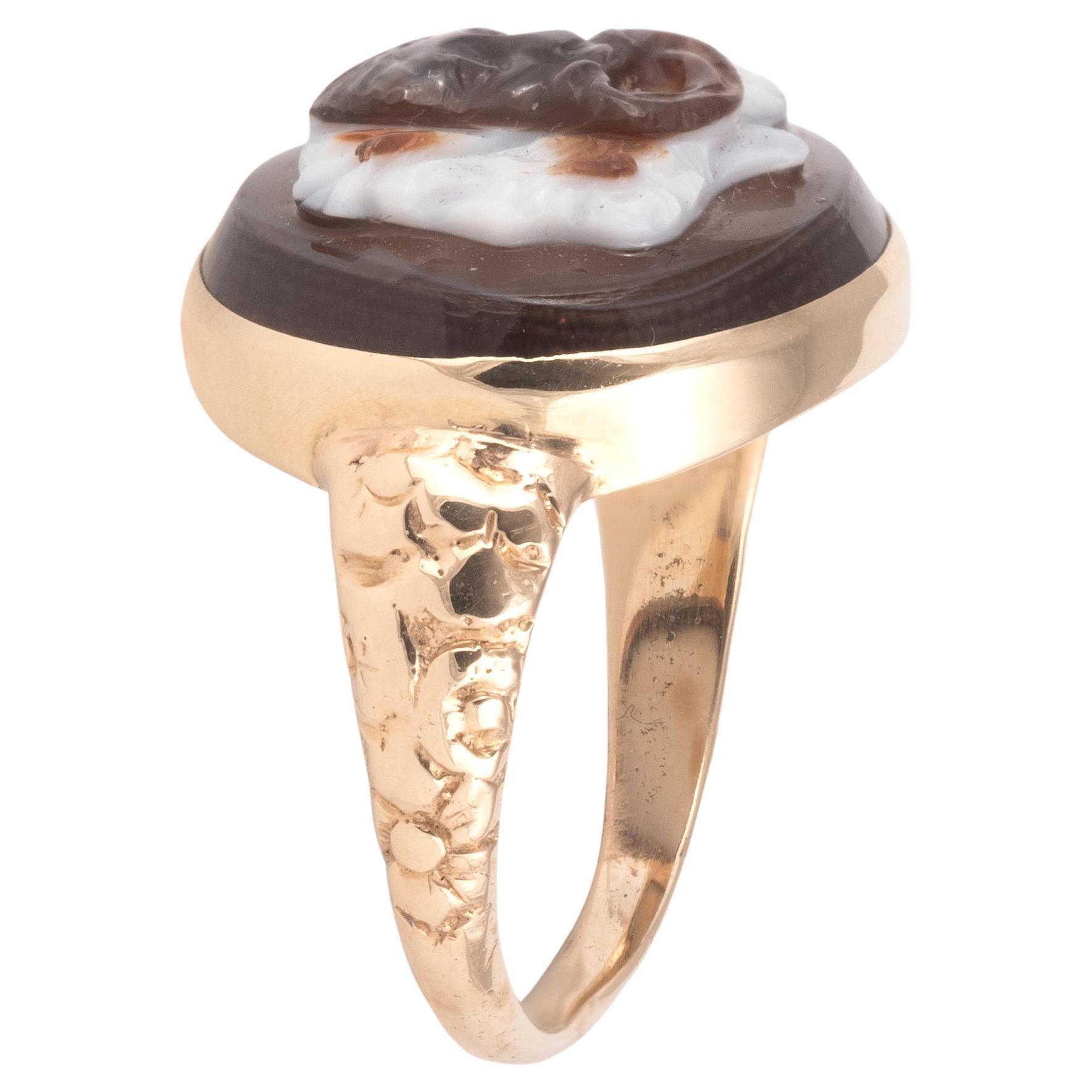 An agate cameo ring, 19th century, set with an oval agate cameo depicting a tragic Greek theatre mask over the double-faced god Janus, to a gold mount with engraved floral shoulders, size 6 1/2 

In Roman mythology, Janus was a king of Latium (a