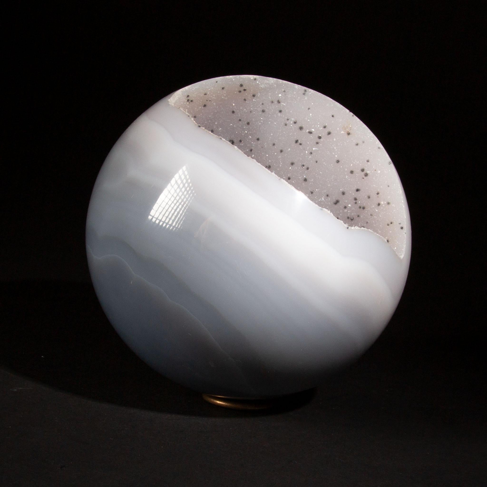 This 5.5-inch Agate Geode Sphere is a remarkable blend of natural beauty and geological intrigue. Polished to a glossy perfection, the exterior showcases the smooth, banded patterns typical of high-quality agate. Within, the sphere reveals a