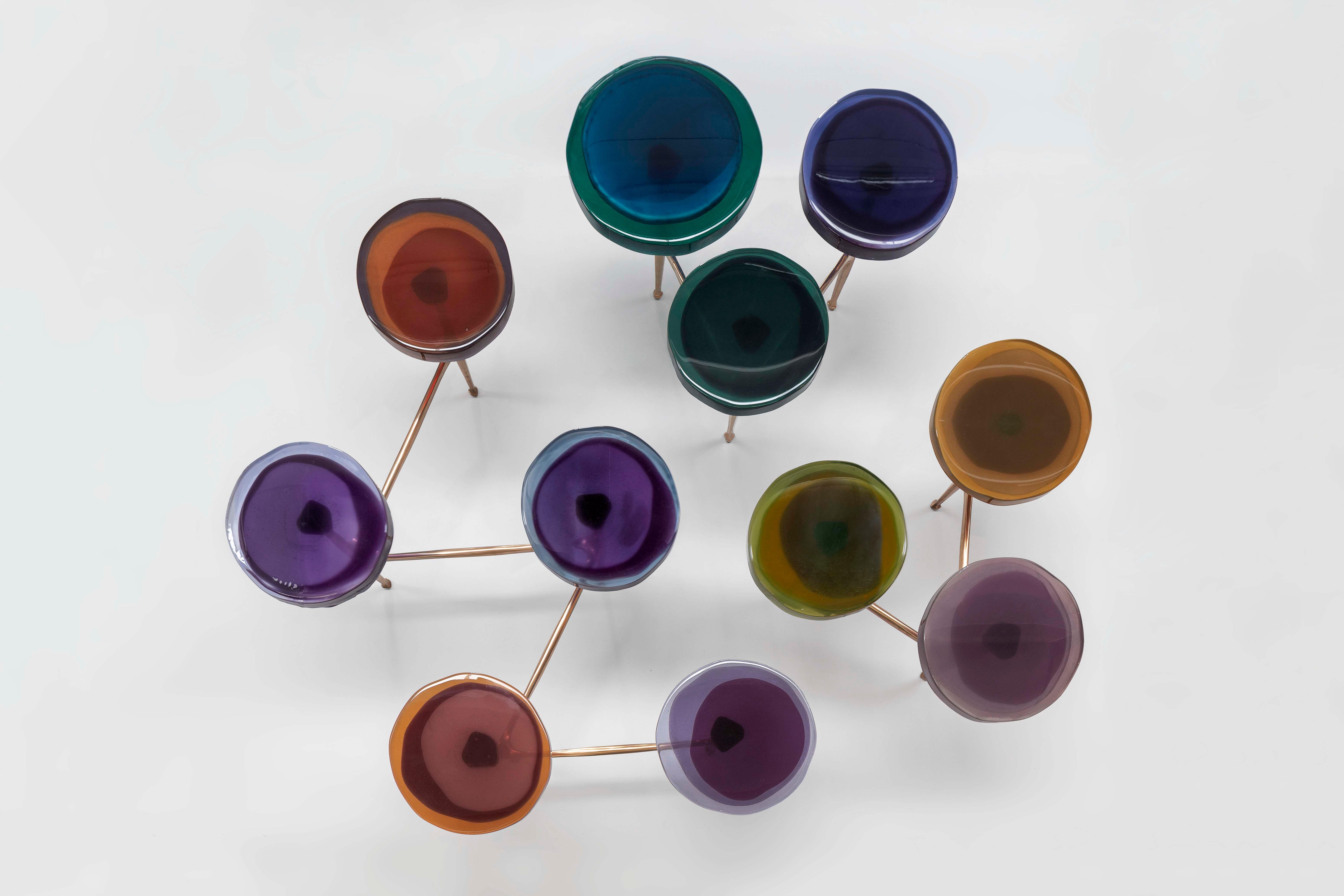 Boasting irregular circular tops made of transparent and colorful resin arranged in a staggered manner on a bronze frame, this organic table draws inspiration from clusters of wildflowers. Crafted using a specialized resin-casting technique, the