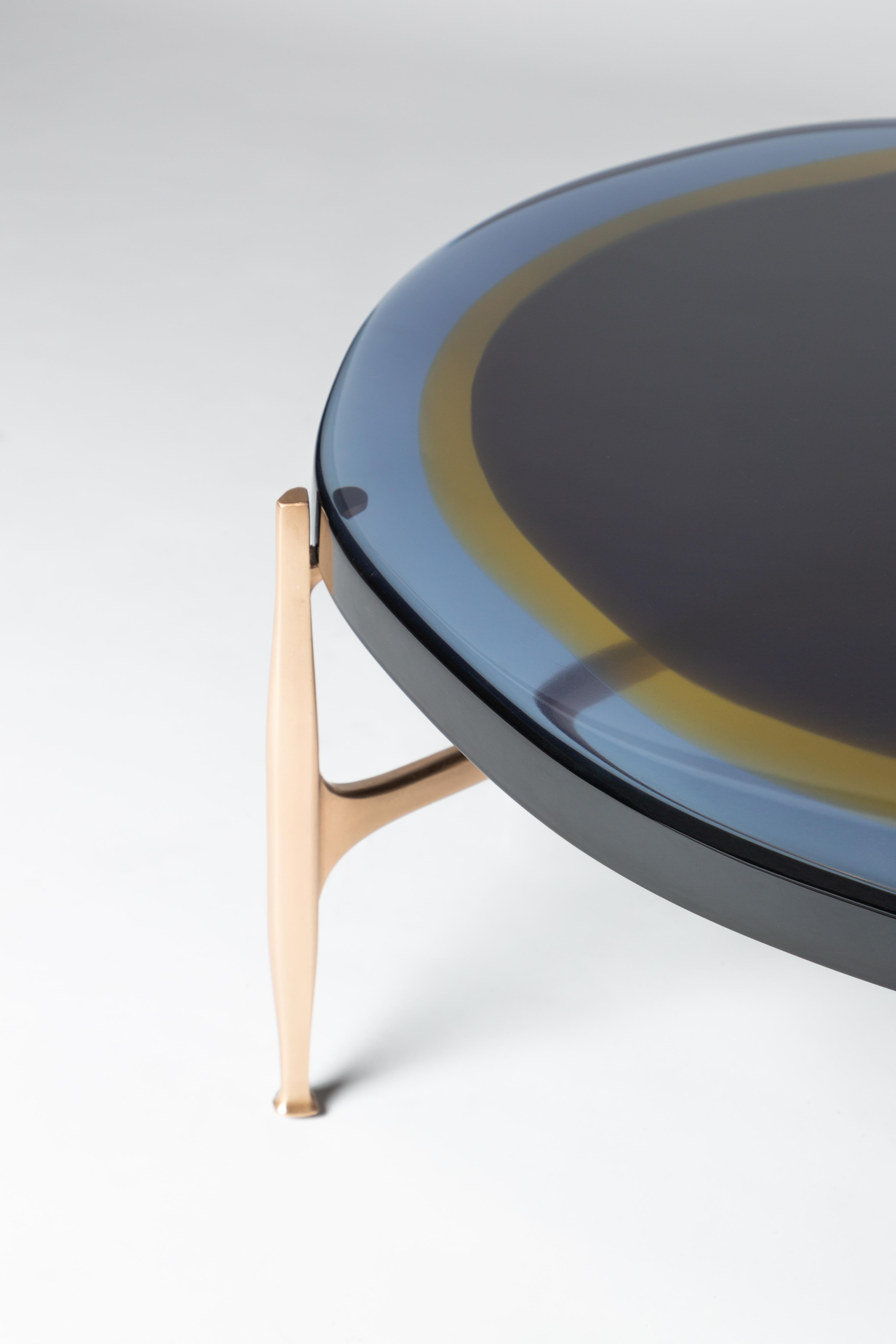 With an irregular circular top crafted from transparent and colorful resin, arranged in a staggered pattern on a bronze frame, this table plays with light. The production process entails a specialized resin-casting technique. The material is layered