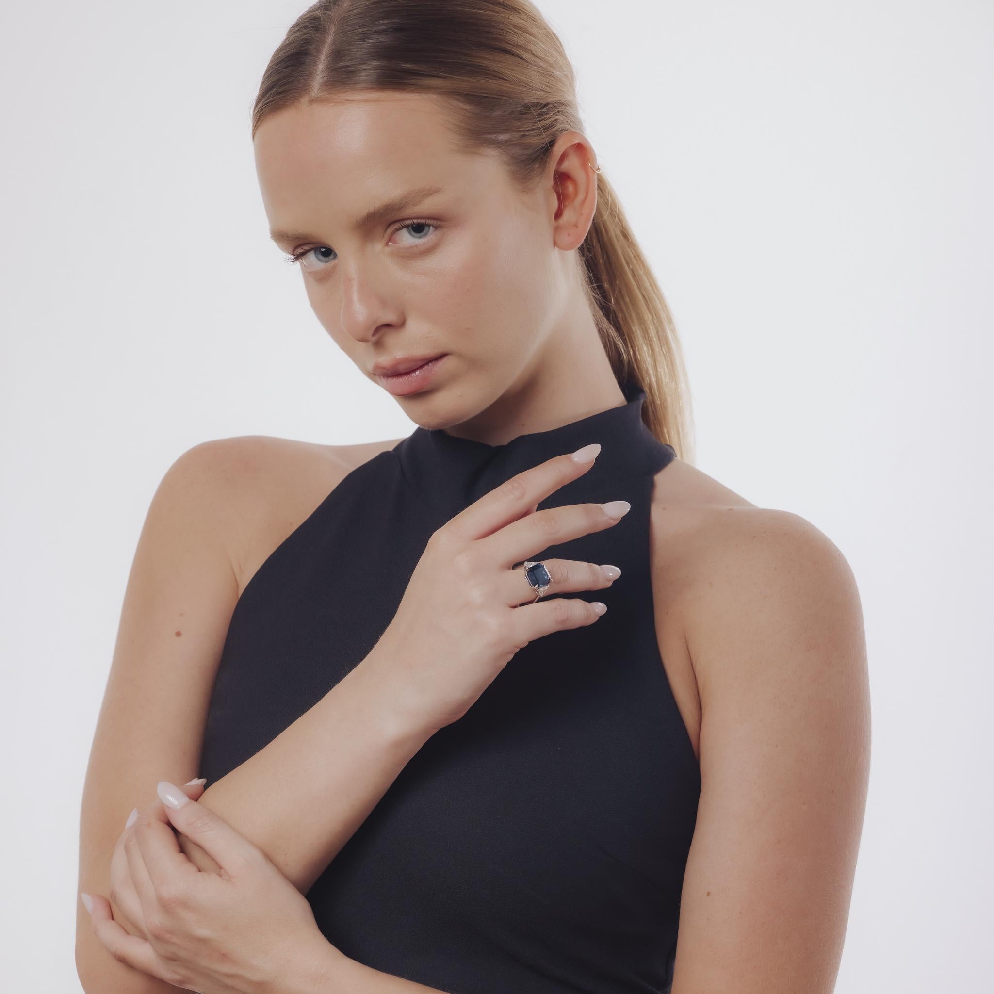 Cette bague contemporaine en platine à trois pierres met en valeur un extraordinaire saphir carré de 9,36 carats d'origine thaïlandaise, taillé en émeraude et certifié non traité pour sa beauté naturelle. Le saphir éclatant est complété par deux