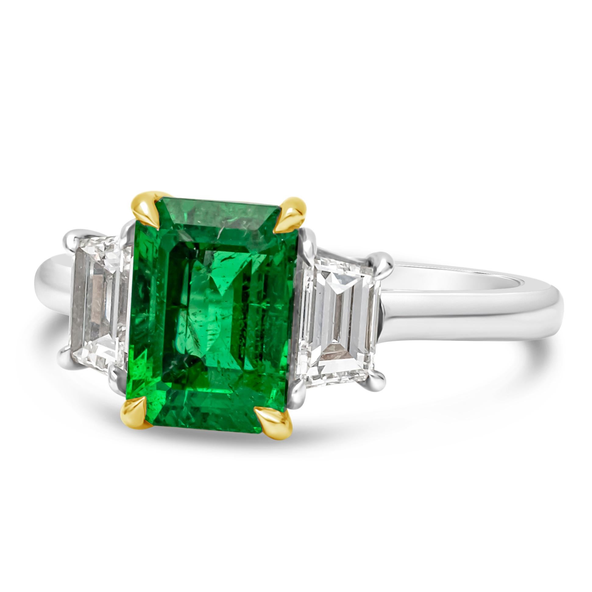 This stunning and elegant engagement ring showcasing a AGL certified color-rich emerald cut green emerald center stone weighing 2.14 carats, VS in clarity and set in a classic four prong basket setting. Flanked by two brilliant trapezoid diamonds on