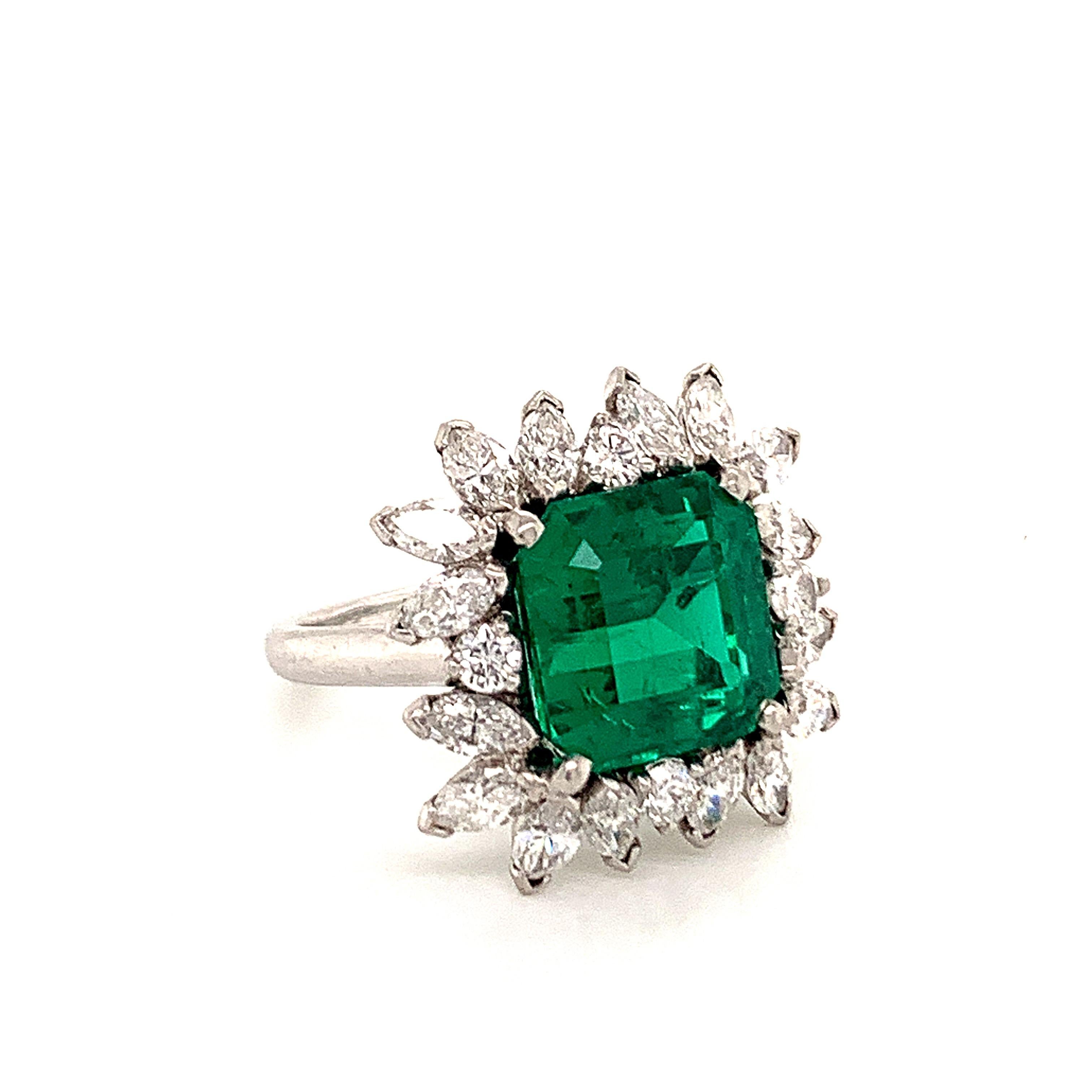 An exquisite AGL certified 5.05 carat Colombian emerald is the glowing star of this fanciful ring. Graded with insignificant oil treatment, the vividly clean emerald is surrounded by 16 marquise cut diamonds and 4 round brilliant diamonds that weigh