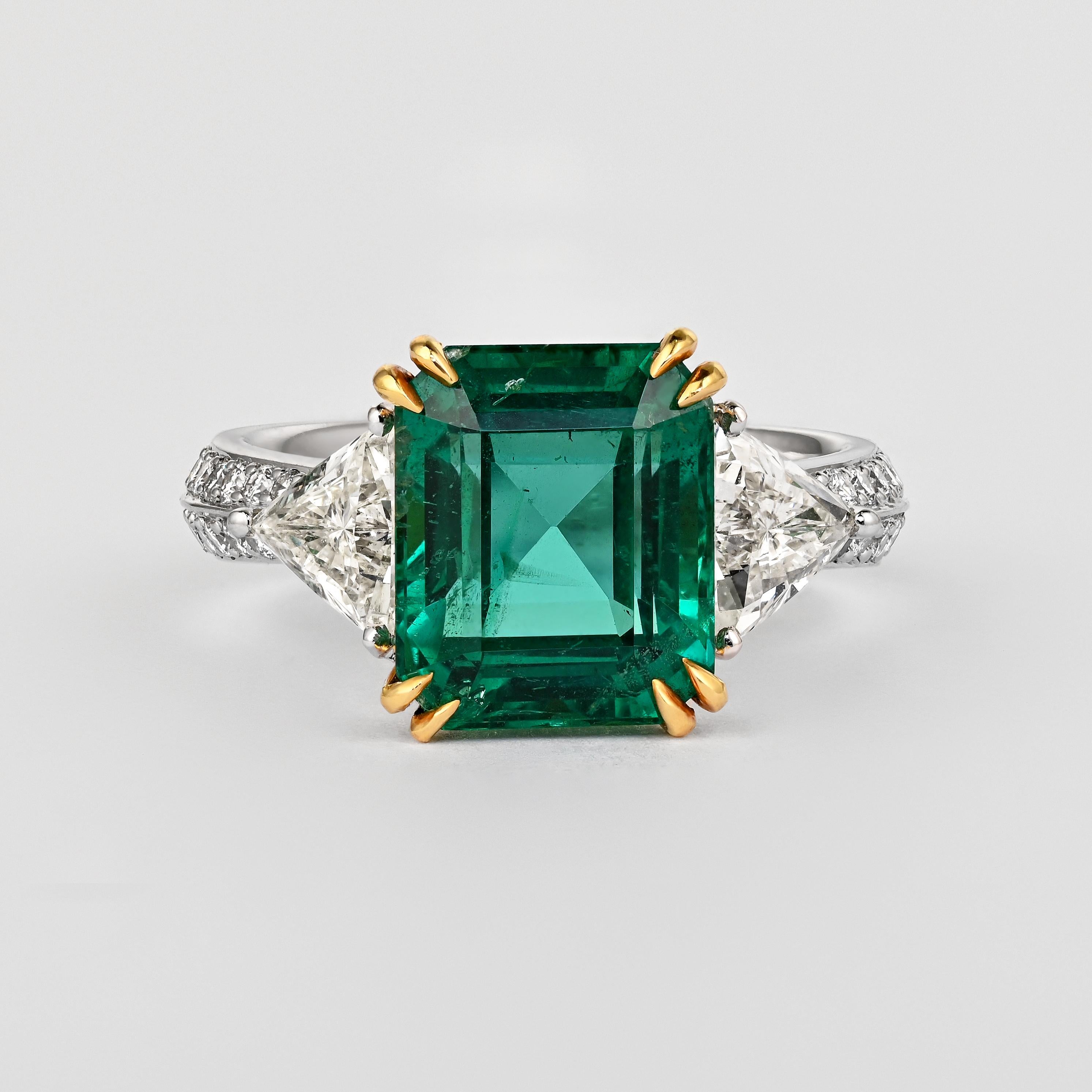 An individualistic statement of love, this three stone engagement ring showcases a natural Brazilian 5.31-carat no oil emerald. The emerald is AGL certified. Additionally, the ring boasts two triangular (trillion) cut white diamonds on each side of