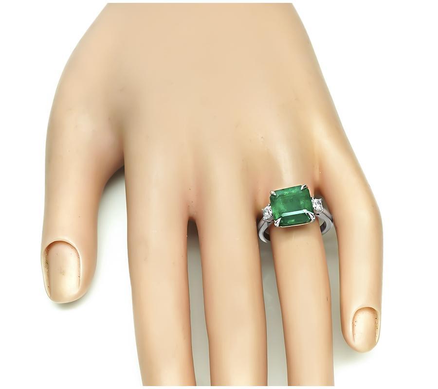 This is a gorgeous platinum engagement ring. The ring is centered with lovely AGL certified emerald cut Zambia emerald that weighs approximately 5.33ct. The center stone is accentuated by sparkling cushion cut diamond accents. The top of the ring