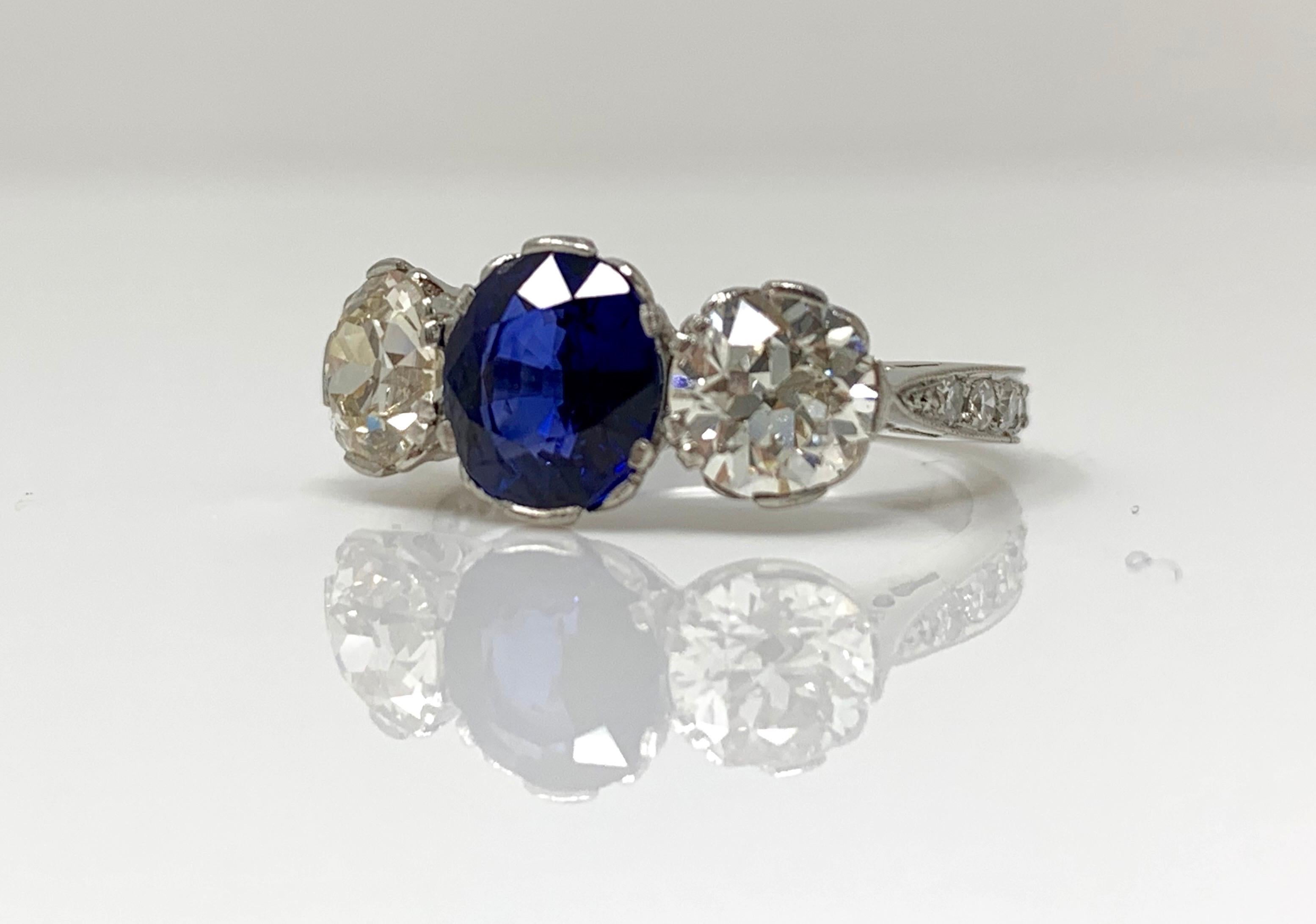 Cette élégante et magnifique bague à trois pierres présente un saphir bleu naturel ovale à taille mixte et des diamants blancs. Les détails sont les suivants : 
Poids du saphir bleu : 1,65 carat 
Diamant blanc taille européenne ancienne poids : 1,60