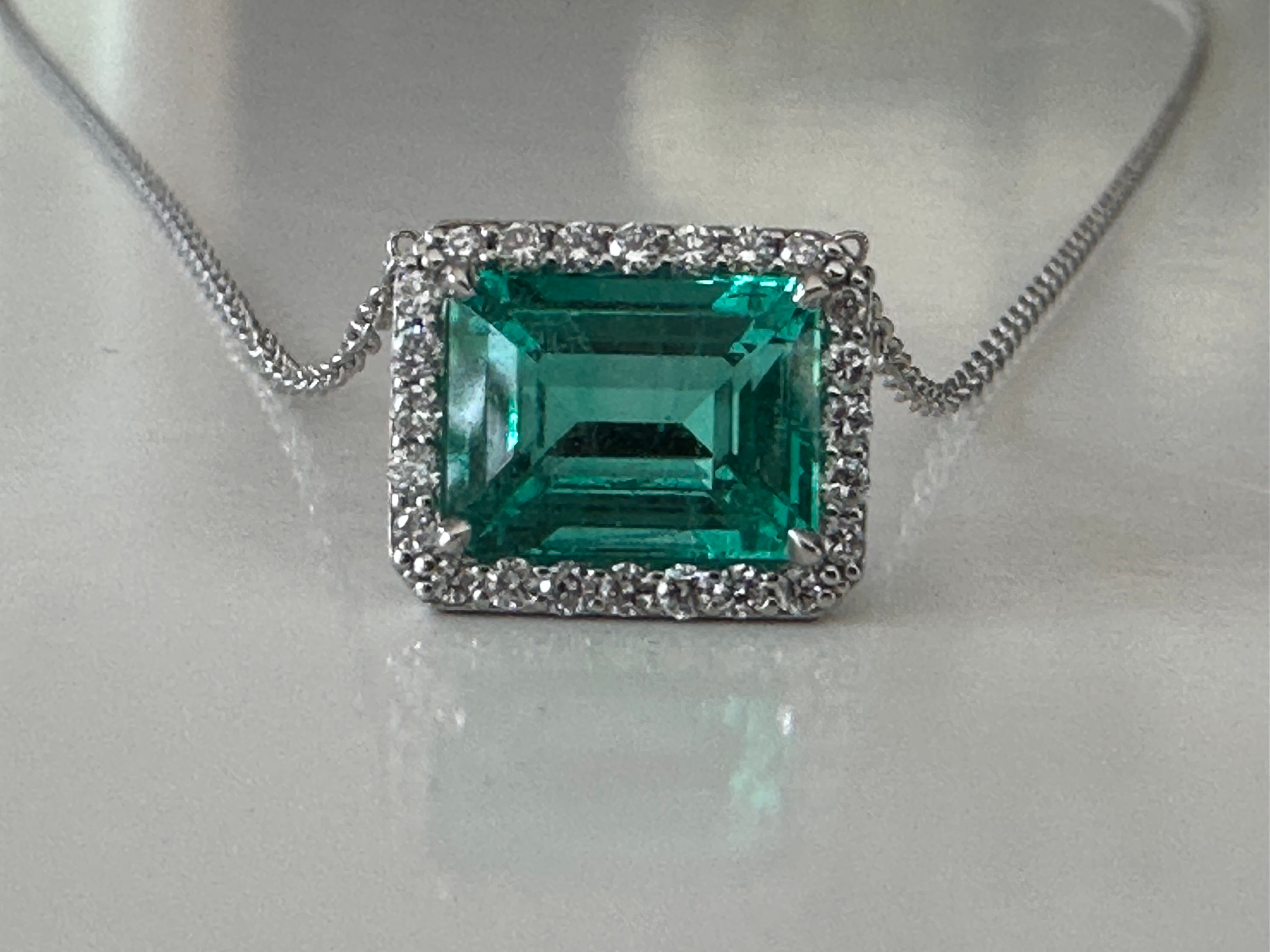 Handcrafted in platinum, this exquisite pendant necklace features a 2.39-carat emerald-shaped Colombian emerald surrounded by a halo of twenty-four round diamonds totaling 0.23 carats, GH color, VS clarity. The emerald is certified by the American