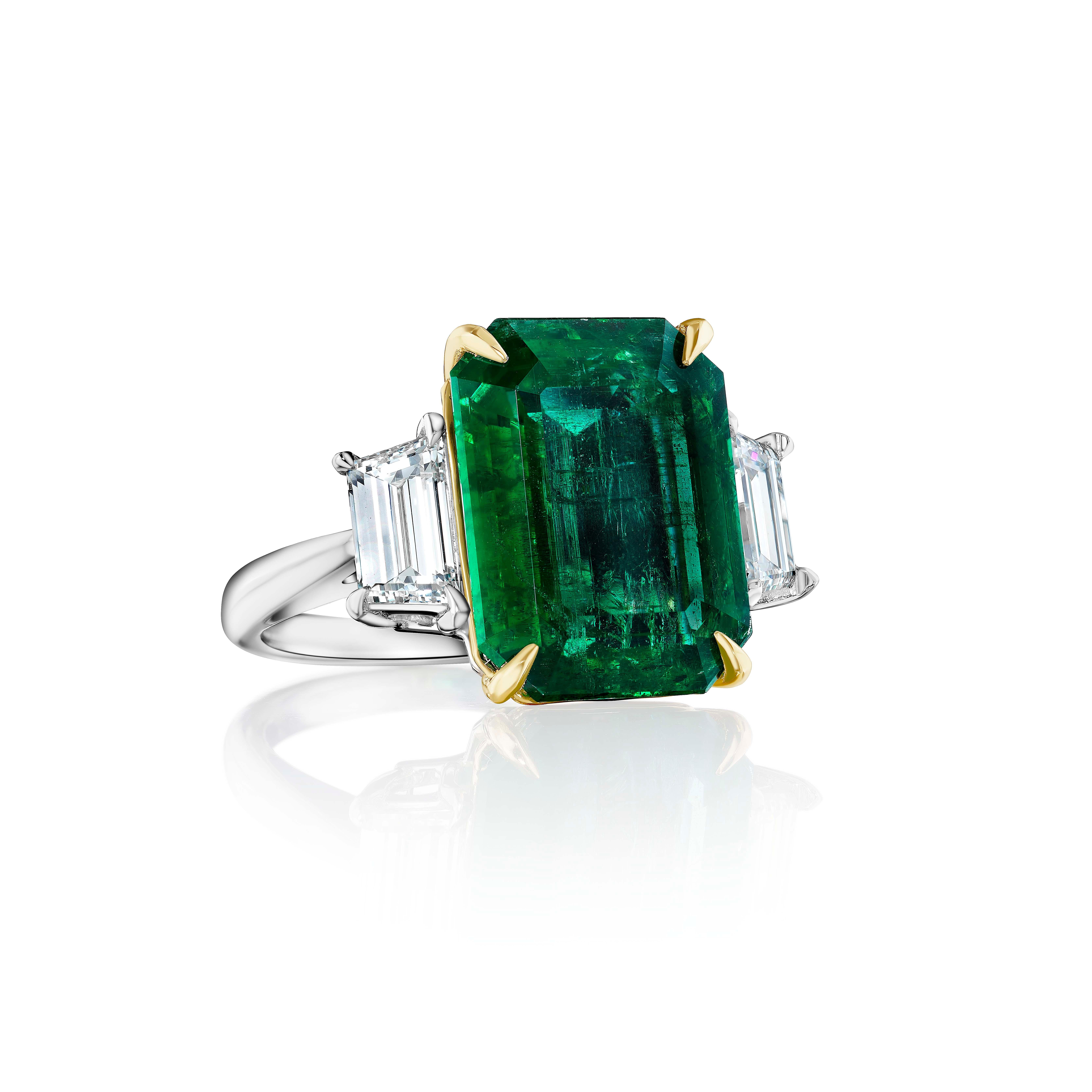 Centered upon a Emerald Cut Emerald weighing 10.08 Carats, flanked by Step Cut Trapezoid Shaped Diamonds weighing 1.43 Carats.

Set in Platinum and 18 Karat Yellow Gold.
Size 6.5