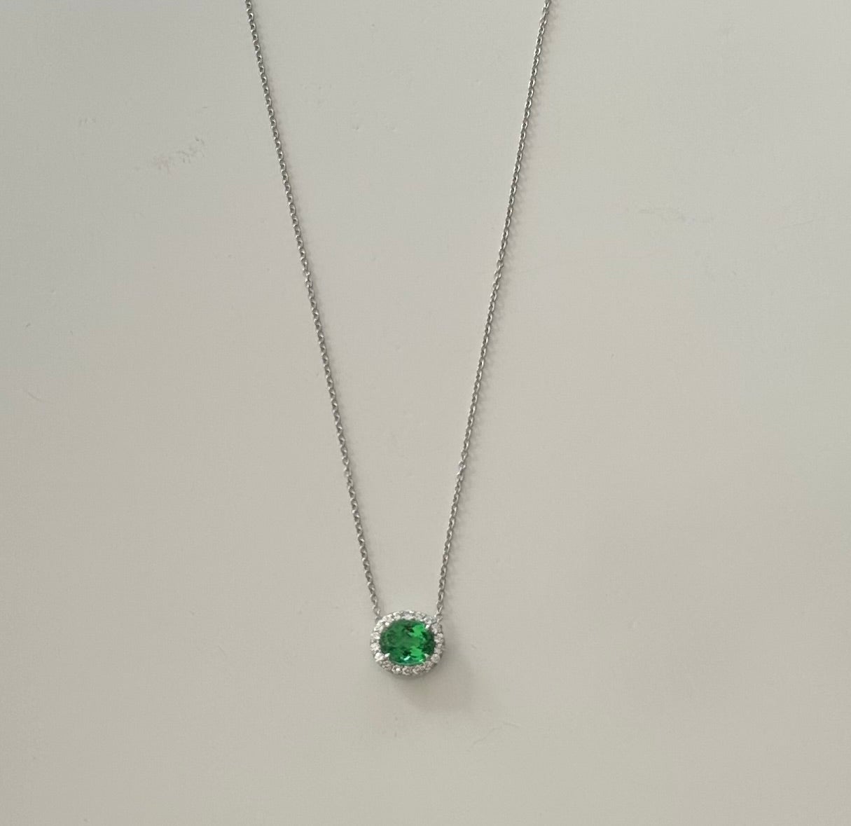 Handcrafted in platinum, this exquisite pendant necklace features a 1.46-carat natural green oval-shaped paraiba surrounded by a halo of eighteen round diamonds totaling 0.18 carats, GH color, VS clarity. The paraiba is certified by the American