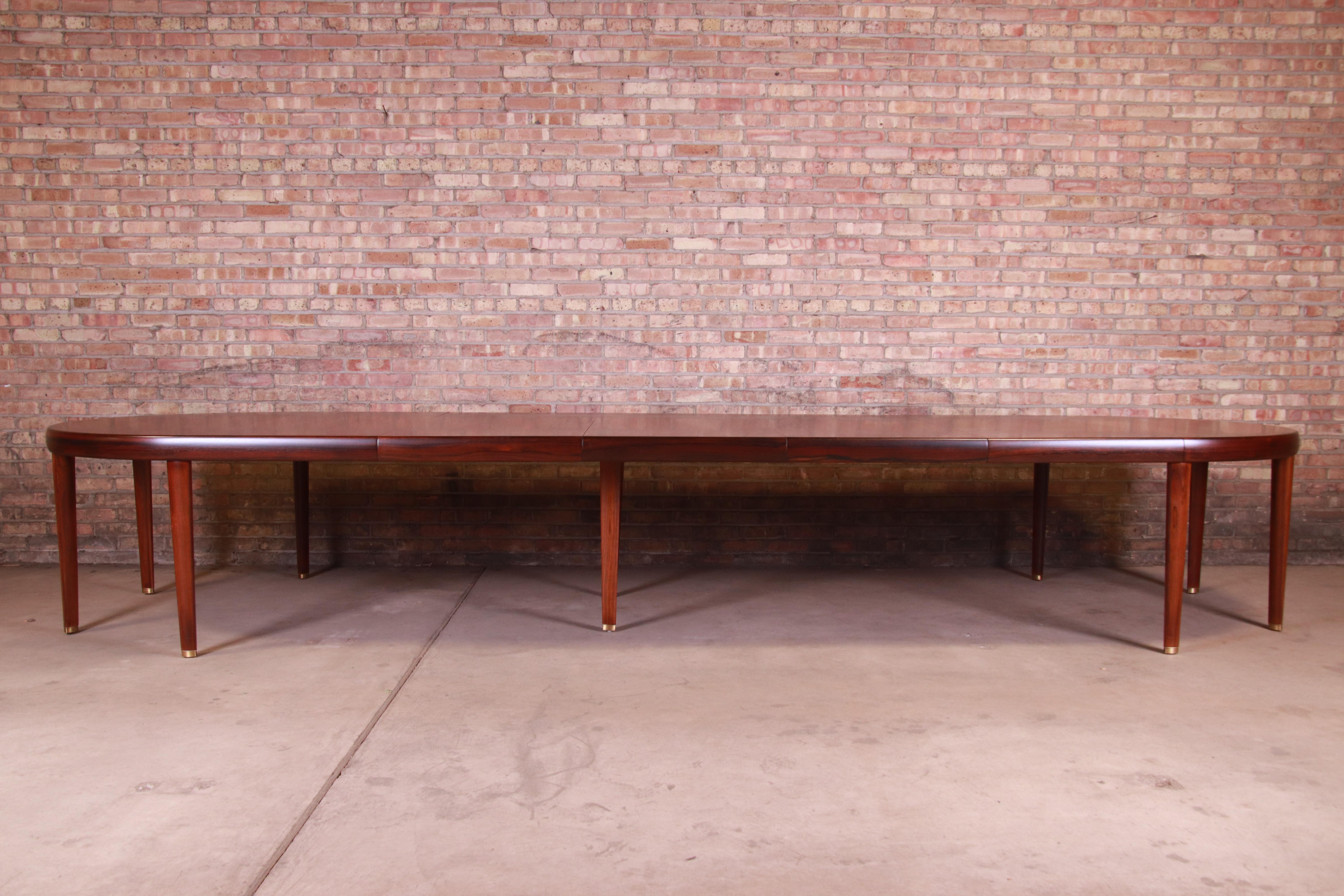 An outstanding midcentury Danish modern extension dining or conference table

In the manner of Agner Christoffersen

Denmark, circa 1950s

Bookmatched rosewood, with brass inlay and brass-capped feet.

Measures: 78.75