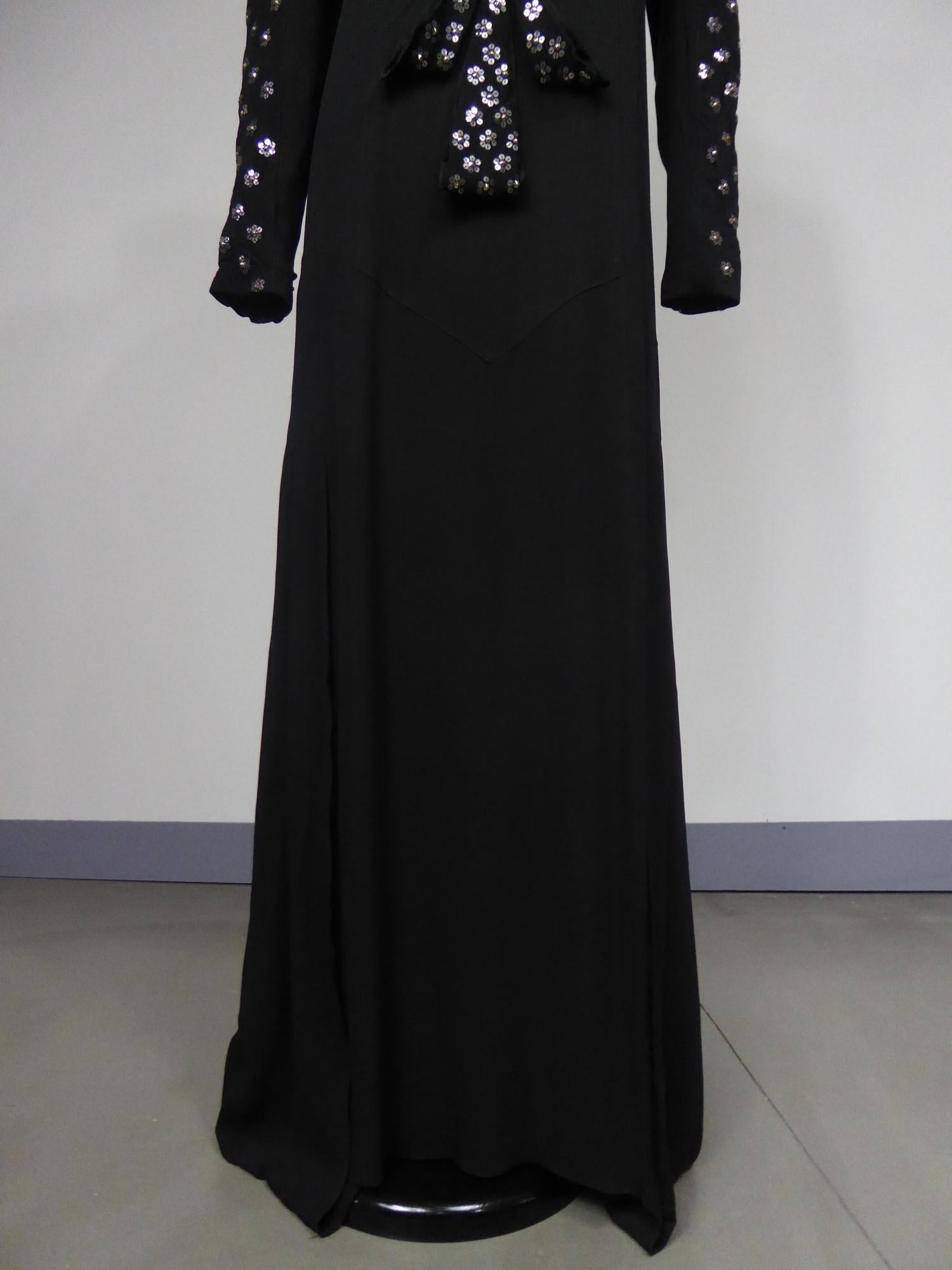 Circa 1932
France

Rare evening dress from Agnès Drecoll designer house in black silk crepe and metallic sequins from the 1930s. Straight crew-neck dress with long sleeves flaring from the hips by pleated flares cut in the bias forming a small train