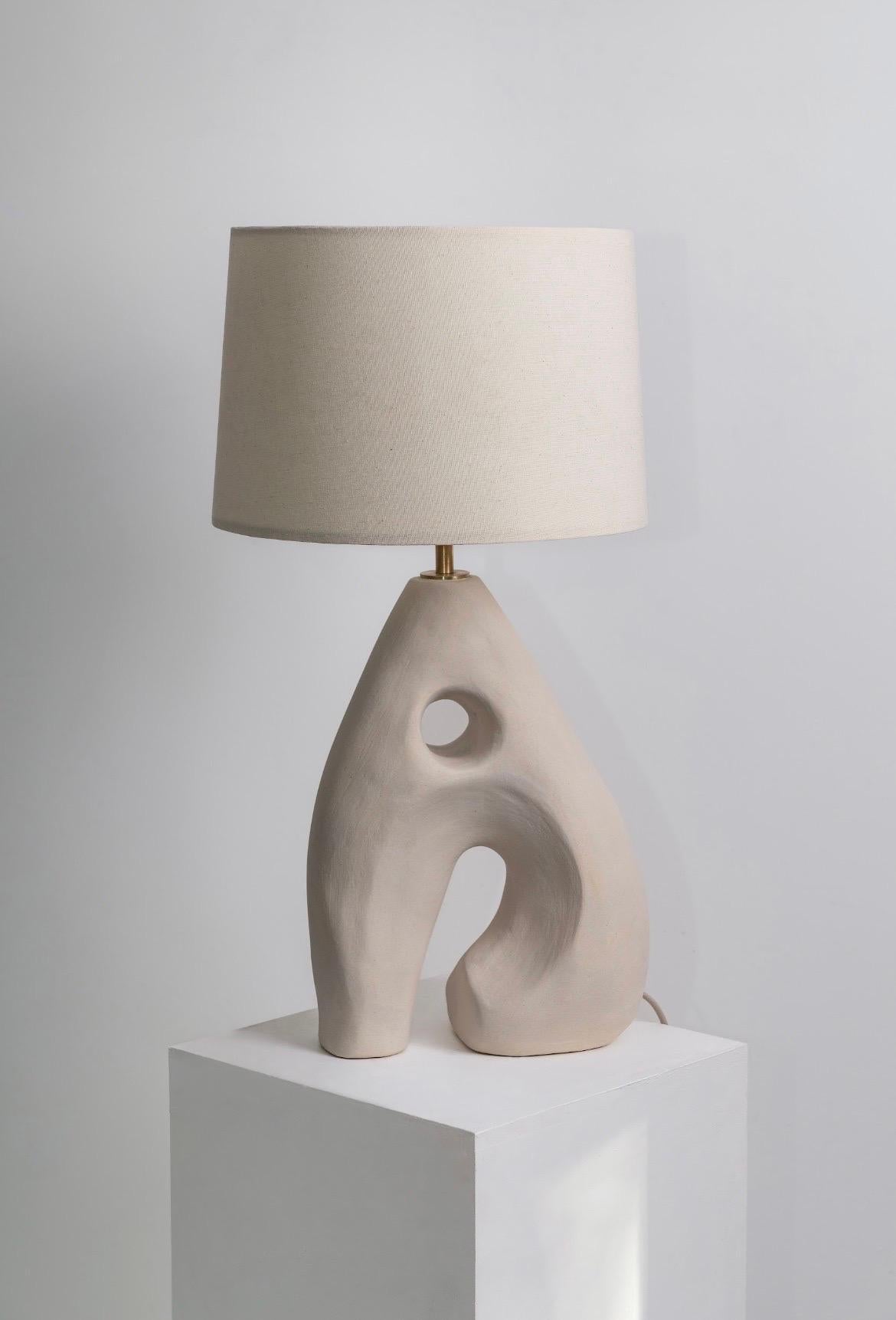 Lampe de table Agnes en céramique sculpturale par Hanna Englund Ceramics.
Dimensions : 30 x H 57 cm
MATERIAL : Grès, céramique, laiton brut, lin.
Lampe à pied sculpturale en céramique, faite à la main, avec un trou de forme organique au milieu. Fait