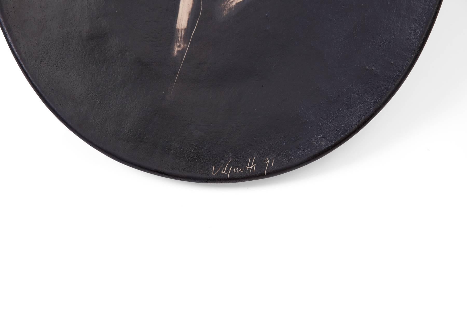 Agnese Udinotti ceramic charger, circa 1991. This example was purchased directly from the artist and has a black painted background with Udinotti's iconic figures in the center. The charger can also be hung on the wall as a sculptural piece. Signed