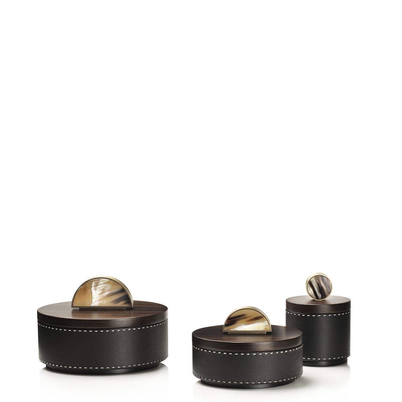 Agneta Box I by Arcahorn
Dimensions: D 13 x H 17 cm
Materials: Leather, wood, brass, horn.

Round box in Aida pebbled leather, Onyx colour with handmade ivory stitching. Lid in matte Amara ebony veneer with round handle in horn and burnished