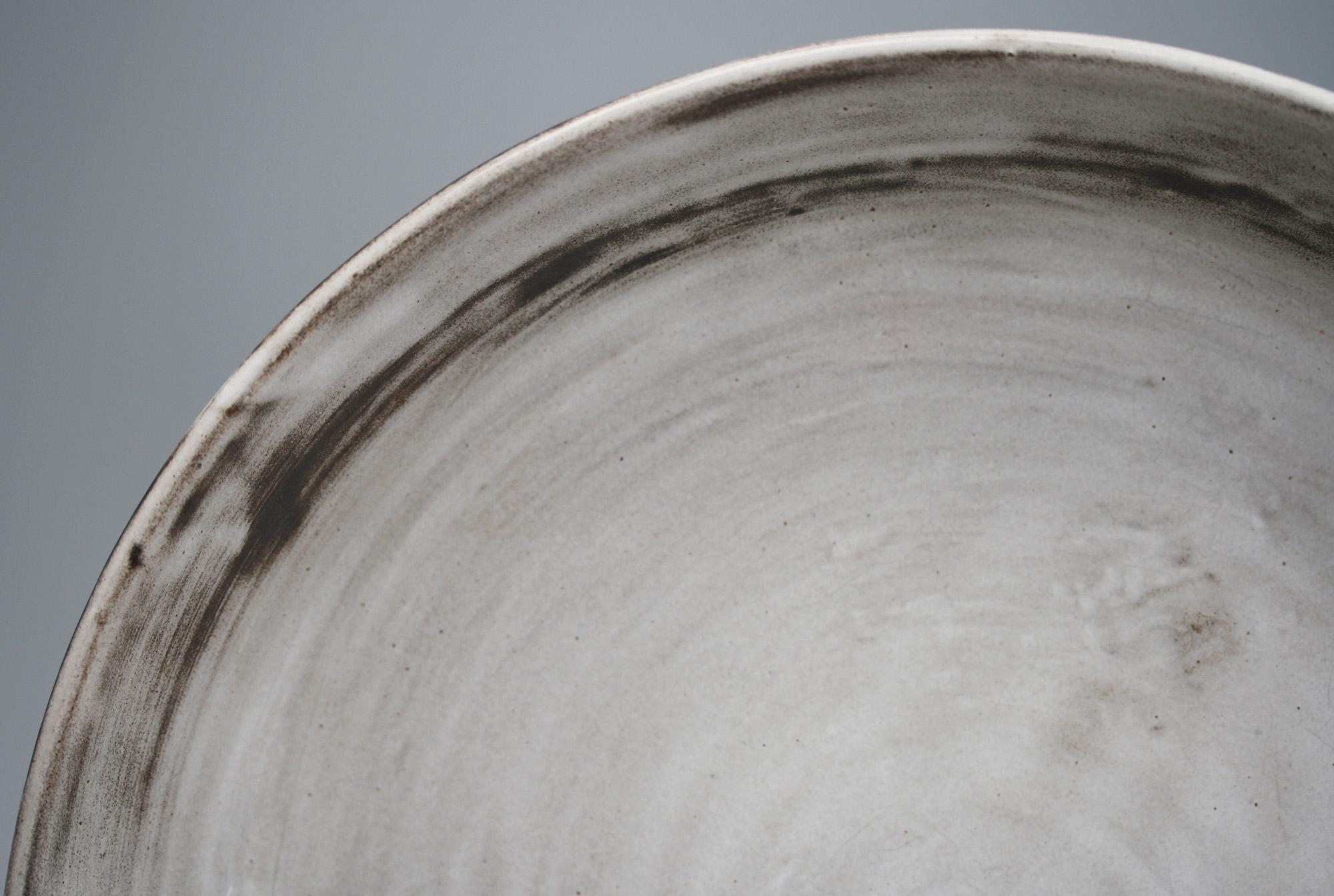 Un beau grand bol vintage en poterie d'atelier peu profond décoré de glaçures à l'engobe gris et noir par Angete Hoy (2014-2000) datant, selon les dires, des années 1950. Le bol est fabriqué à partir d'une argile rouge et présente une forme large,