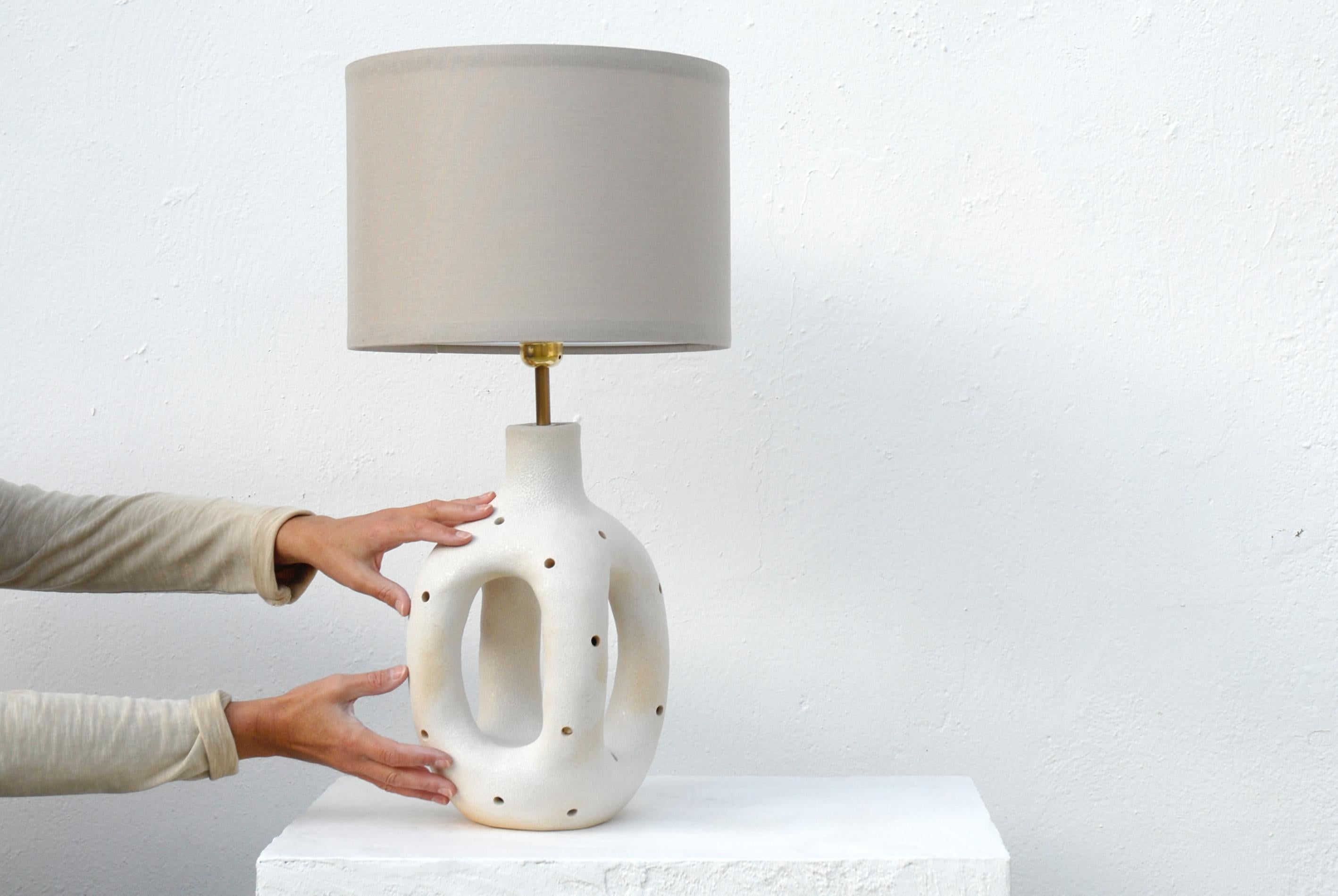 I meticulously handcrafted this unique lamp base, skillfully shaping it from high-quality white stoneware clay. What sets this lamp apart is the whimsical touch I've added by pinching playful holes into the surface. To enhance its visual appeal, I