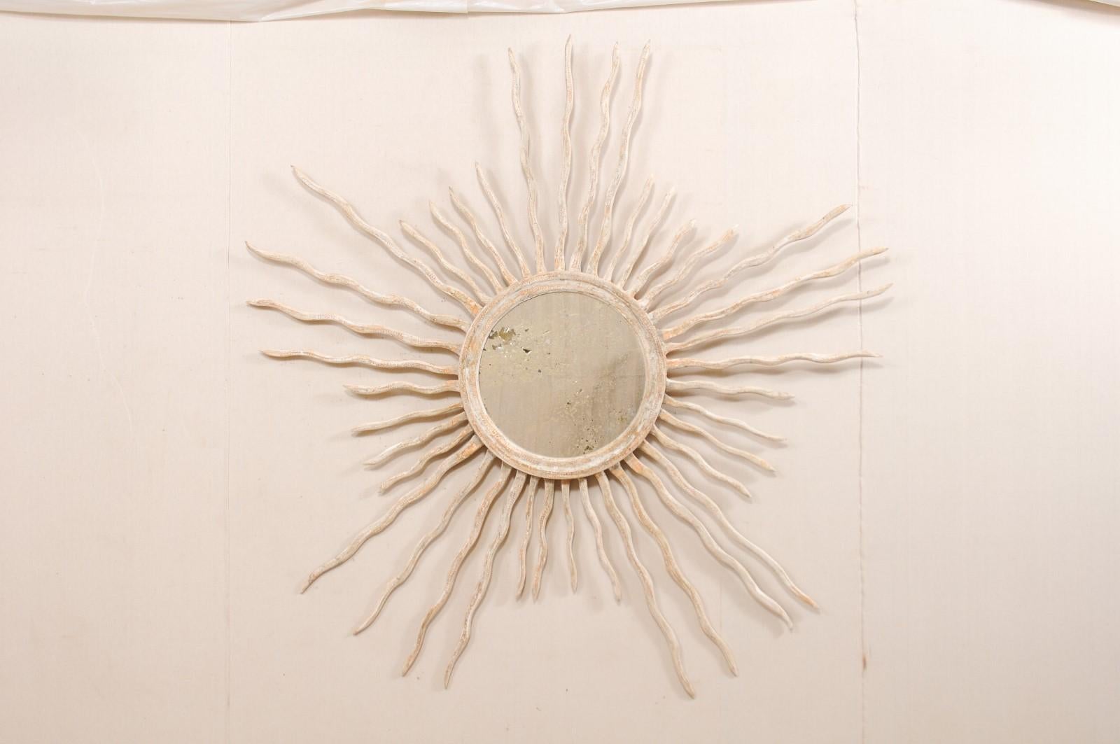 A large sized Italian round mirror with sunburst surround. This custom mirror from Italy, designed by an artisan crafter, features a round-shaped and antiqued center glass, with is set within a wood surround which bursts with rays extending outward