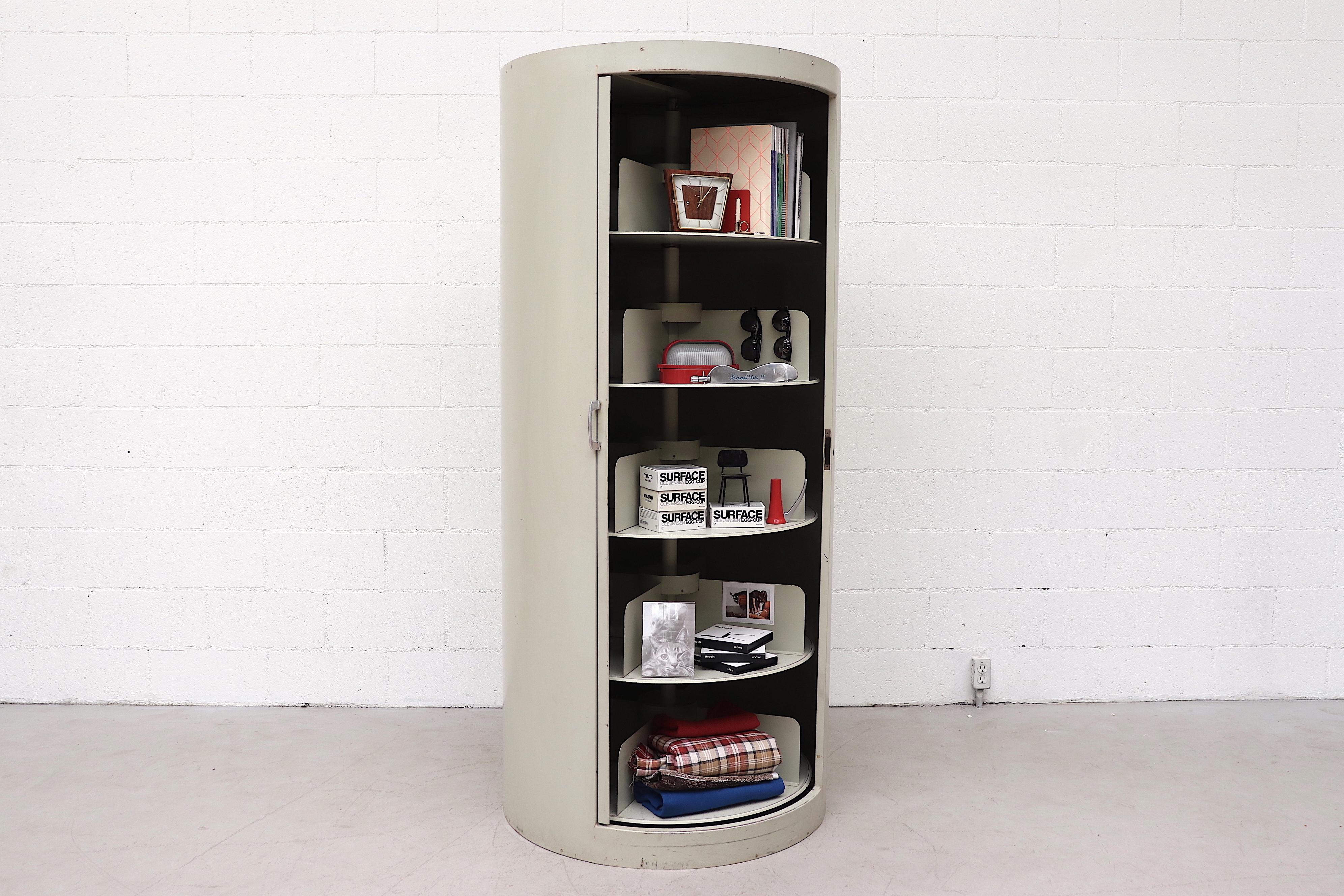 Rare industrial storage unit with 5 rotating shelves and sliding door. Cylindrical grey enameled metal frame in very original condition with visible signs of wear including some denting, scratching and light surface rust and enamel loss.
