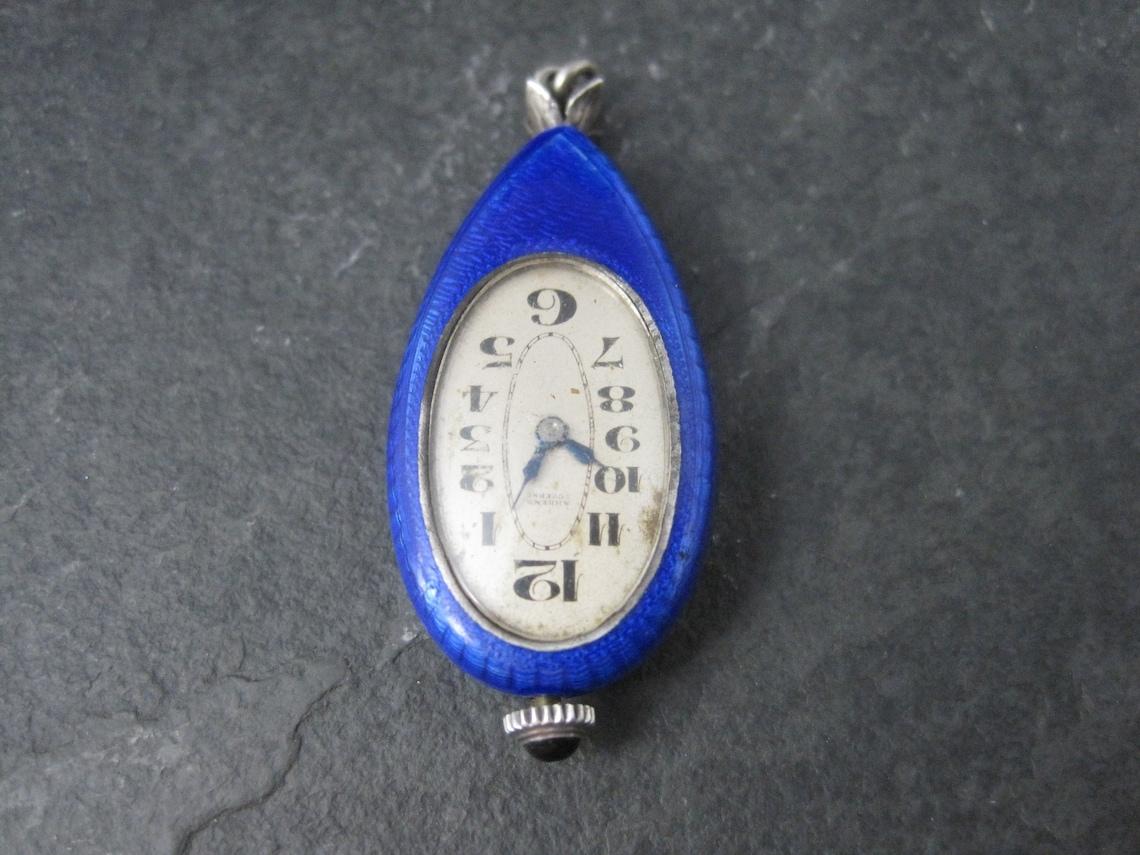 This gorgeous art deco Ahrens Lucerne watch is sterling silver with blue enamel.
It is the mechanical type and keeps time perfectly.

Measurements: 3/4 by 1 11/16 inches

Marks: Sterling Silver SW, Argent 100P, 0.935
Etched A1037

Condition: Inside