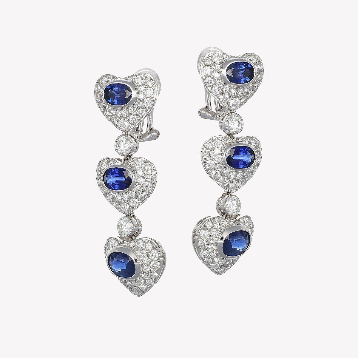 In the radiant embrace of these heart-shaped drop earrings, passion and promise merge into a design of loving hearts. The deep blue sapphires, as profound as the night's veil, are framed by pavé diamonds that shine with pure, vibrant light. Wearing