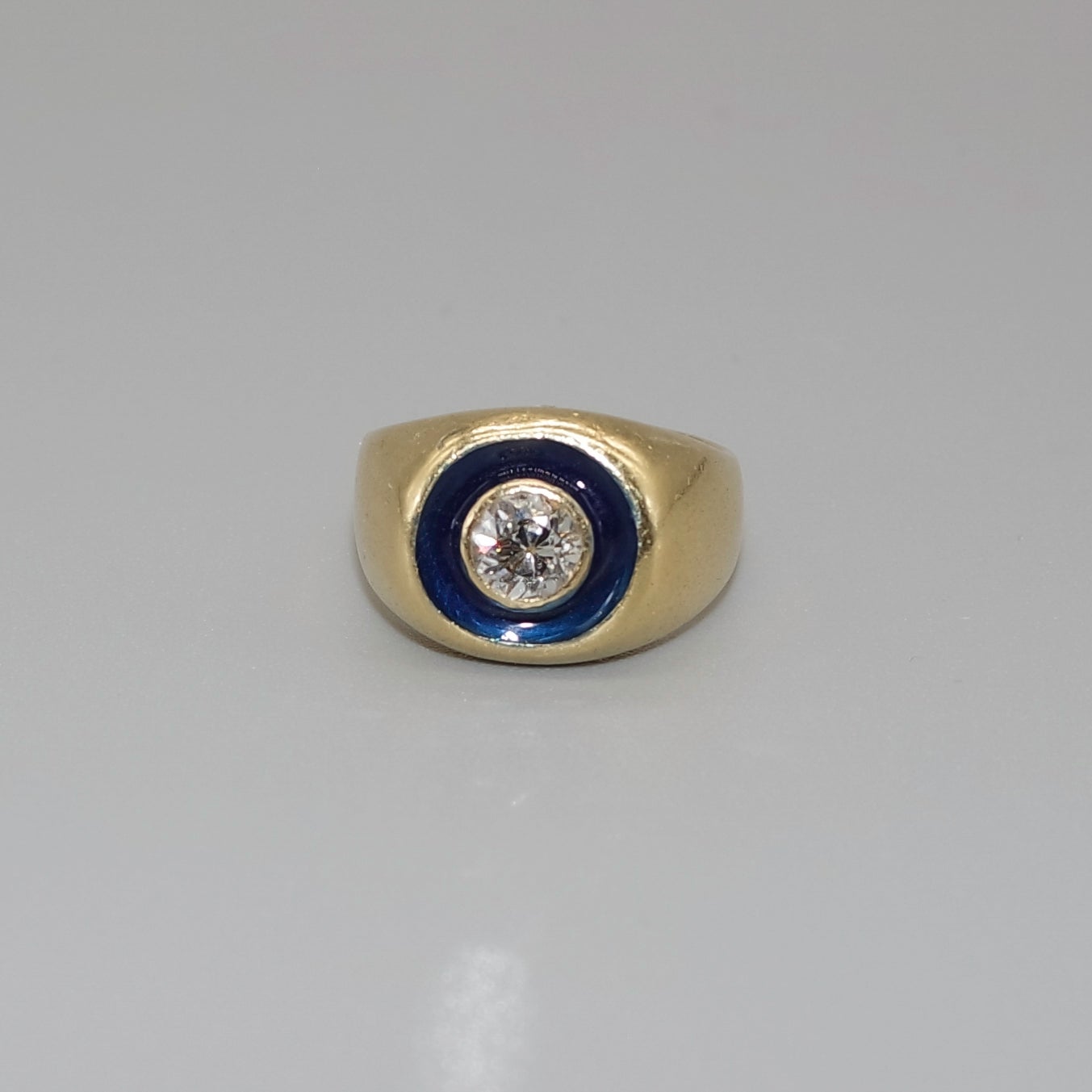 An elegant cluster ring , or chevalière, in 18 karat yellow gold, 1 central natural diamond and blue enamel. 
The creative is inspired by the art déco style, using the color contrast - dark blue enamel verse colorless diamond - as the main stylistic