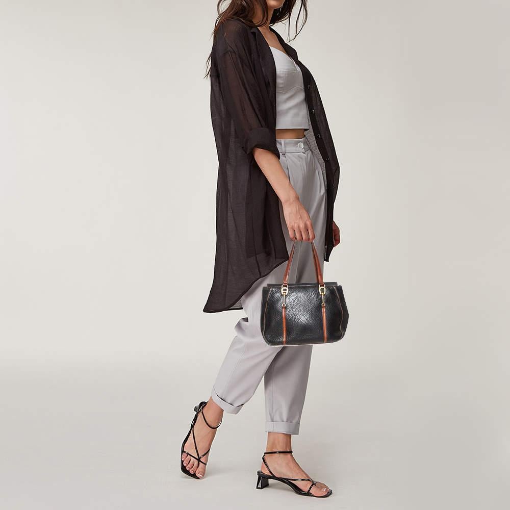 An absolute delight to carry on any day, this tote is an Aigner creation. Crafted from grained leather, the bag features a black shade, two brown handles held by logos, and an interior sized perfectly to hold your essentials. This bag is a must-have.