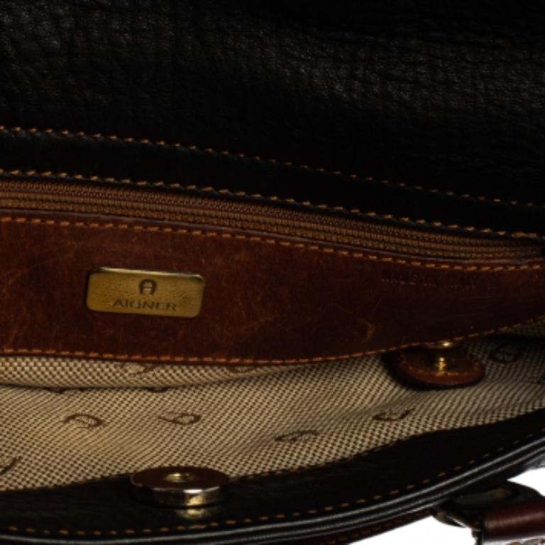 An absolute delight to carry on any day, this tote is an Aigner creation. Crafted from grained leather, the bag features a black shade, two brown handles held by logos, and an interior sized perfectly to hold your essentials. This bag is a must-have.