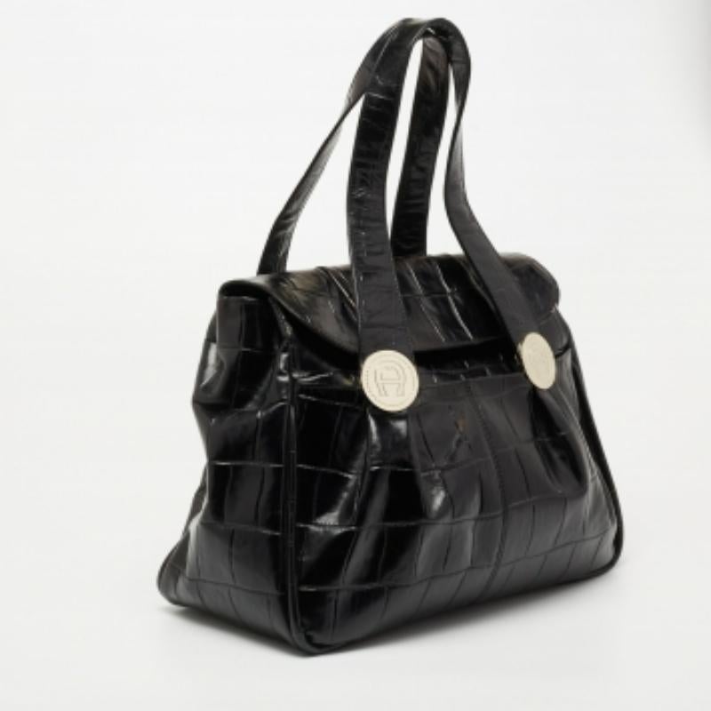 Das moderne Design dieser Aigner-Tasche ist jeden Cent wert. Sie ist aus Leder mit Krokoprägung gefertigt und mit Markenmotiven an den beiden Griffen und goldfarbenen Beschlägen versehen. Der geräumige, mit Stoff gefütterte Innenraum ist mit einer