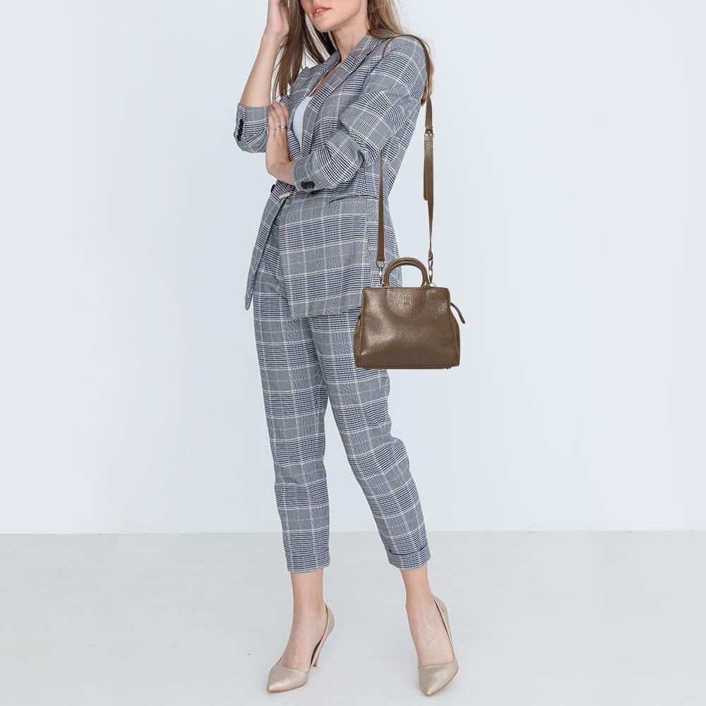 Die Cybill-Tasche von Aigner zeichnet sich durch ihre strukturierte, trapezförmige Form aus und verkörpert Eleganz, Charme und Raffinesse. Sie ist aus genarbtem Leder in einem zeitlosen, dunkelbeigen Farbton gefertigt und minimalistisch mit einem