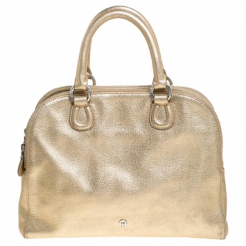 Be the talk of the town when you carry this Aigner handbag. Crafted with leather, this bag is styled with metallic gold hue all over, a top-zip closure and twin top handles. This chic satchel has an equally divine interior lined with fabric. This
