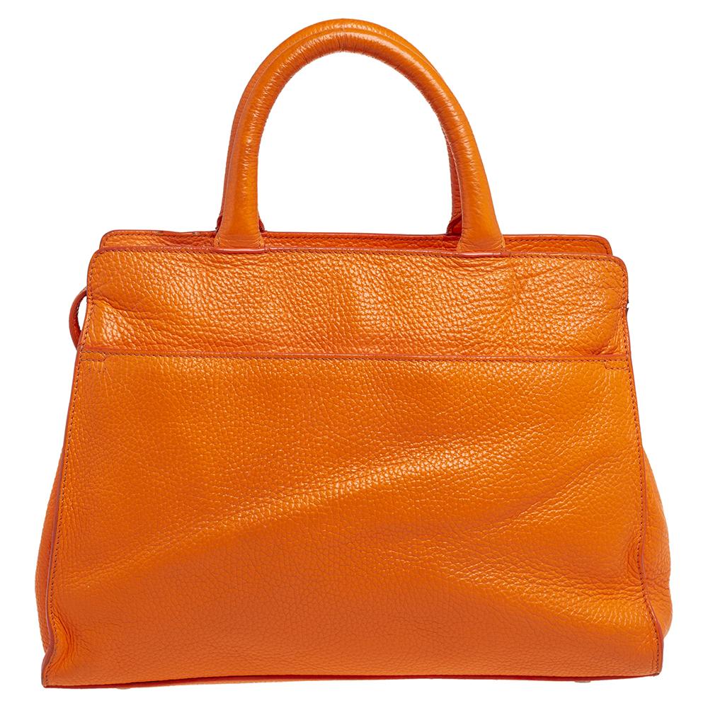 Characterized by its structured, trapezoidal shape, this Cybill tote by Aigner personifies elegance, charm, and sophistication. It is made from leather flaunting an orange shade and is designed minimally with a petite logo at the front in