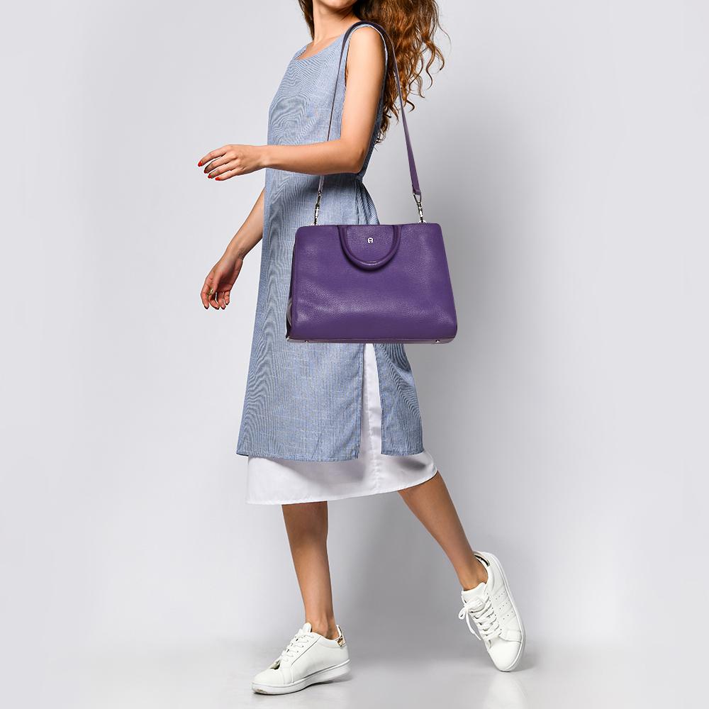 Characterized by its smart, spacious shape, this Cybill tote by Aigner personifies elegance, charm, and sophistication. It is made from leather flaunting a purple shade and is designed minimally with a petite logo at the front in silver-tone and two