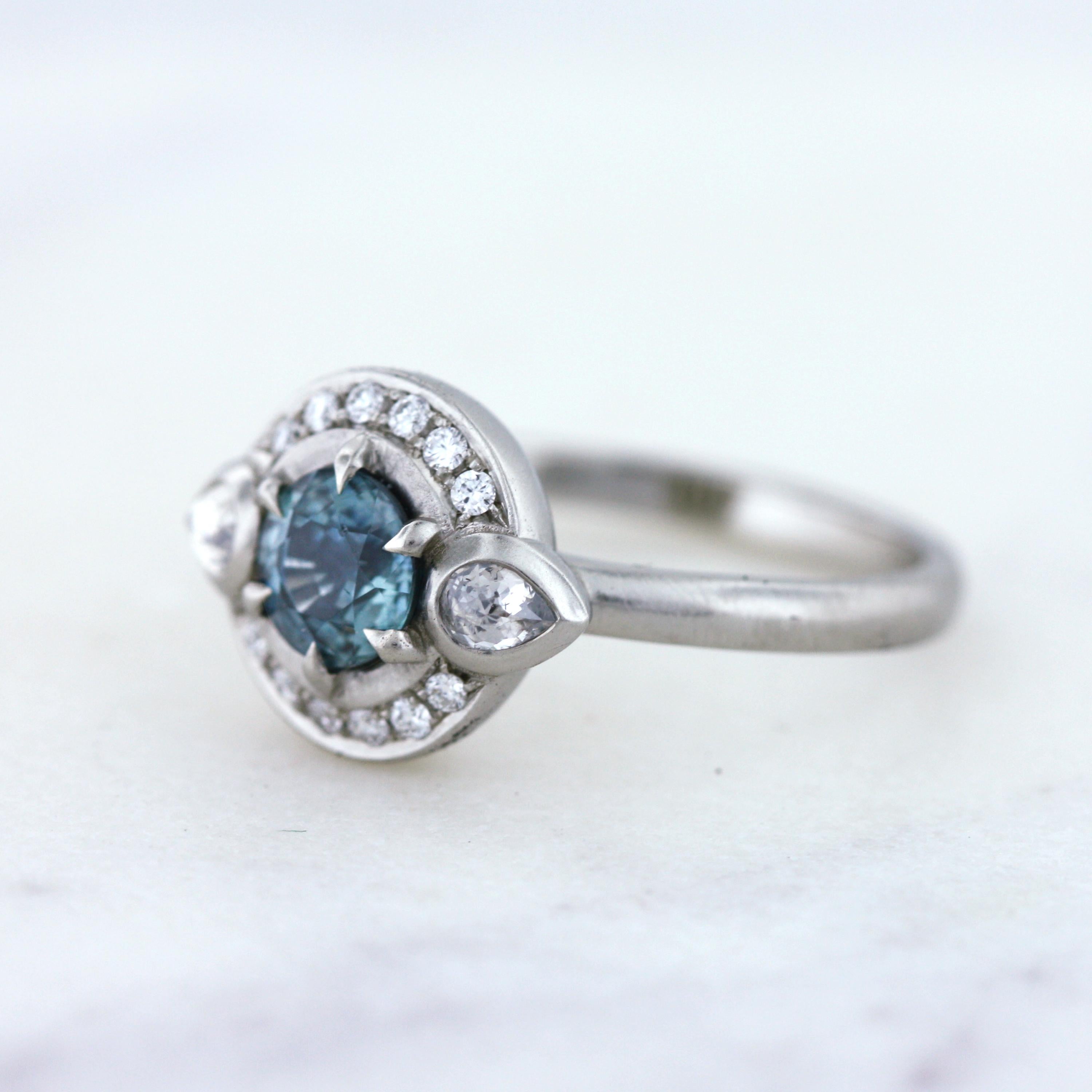 Modern Art Deco inspired ring with a .77 carat teal Montana sapphire and rose cut pear Canadian accent diamonds. All set in 100% recycled 14K white gold. The prefect ring for a American/Canadian couple.
 
- One of a kind
- Finger size 6.25
-