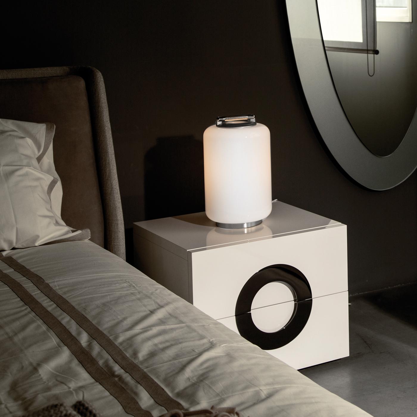 This small and stylish table lamp emits soft, relaxing light through the striking cylindrical diffuser of hand-blown white Murano glass. Resting upon a low, round base made of satin nickel metal, the small size and understated silhouette of this