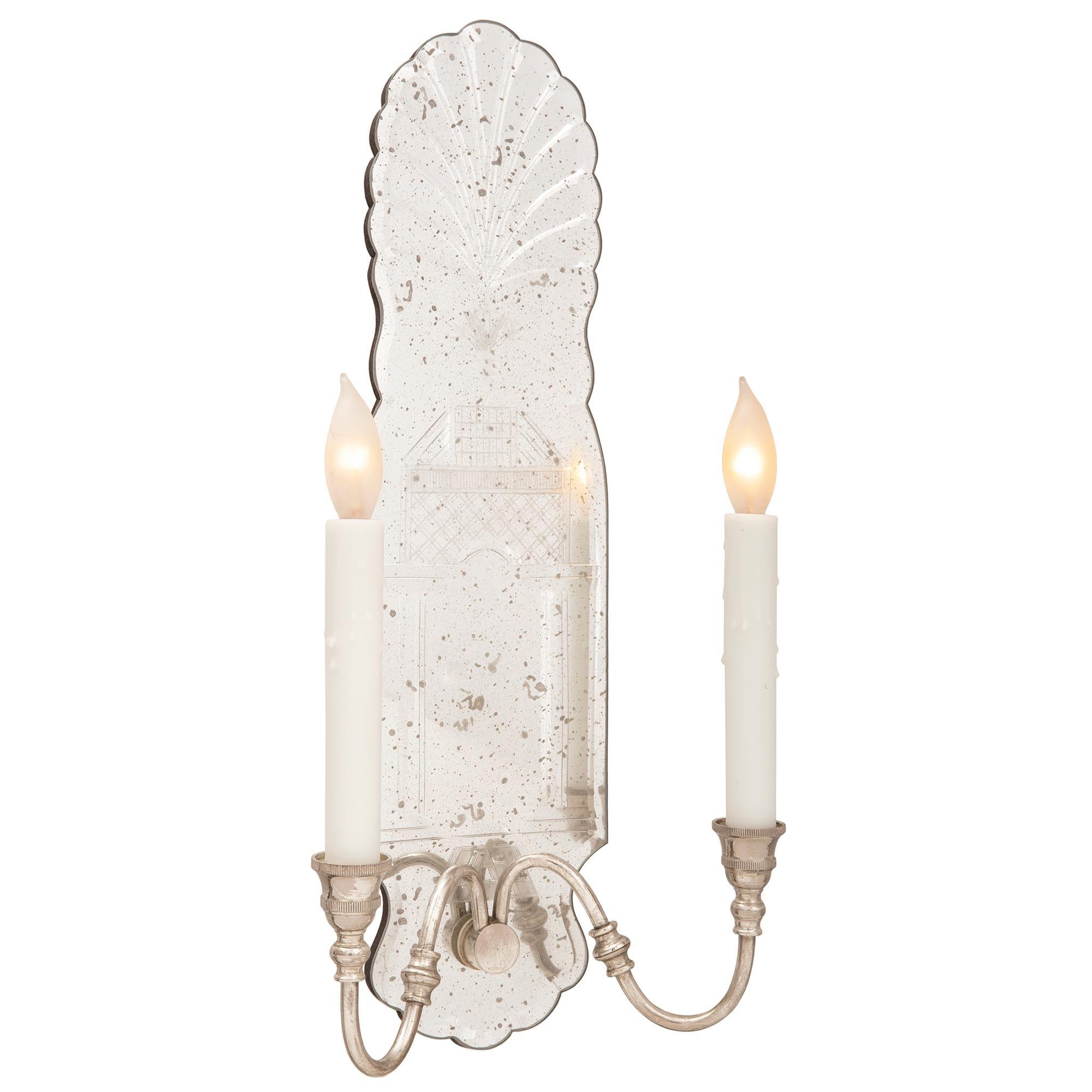 A decorative pair of Italian 20th century Venetian st. silvered bronze and etched glass sconces. Each sconce displays two S scrolled electrified arms ending with a mottled candle cups and two reeded bands. The scalloped shaped etched mirror