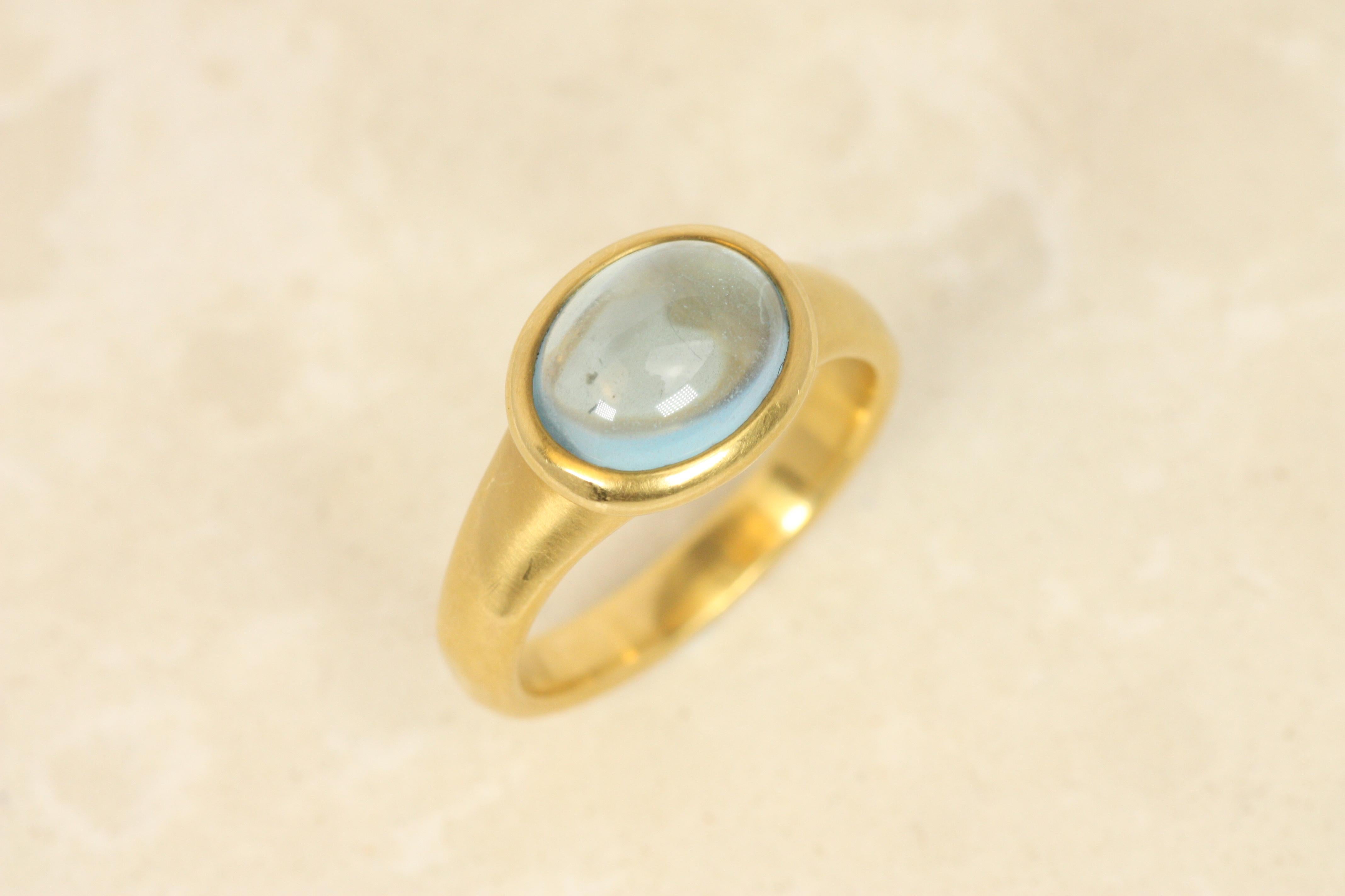 This serene cabochon aquamarine ring captures an airy elegance with its light blue stone, while the 22K yellow gold bold bezeled setting provides a grounding, earthy contrast. The hammered finish on the bezel and band evokes an ancient aesthetic,
