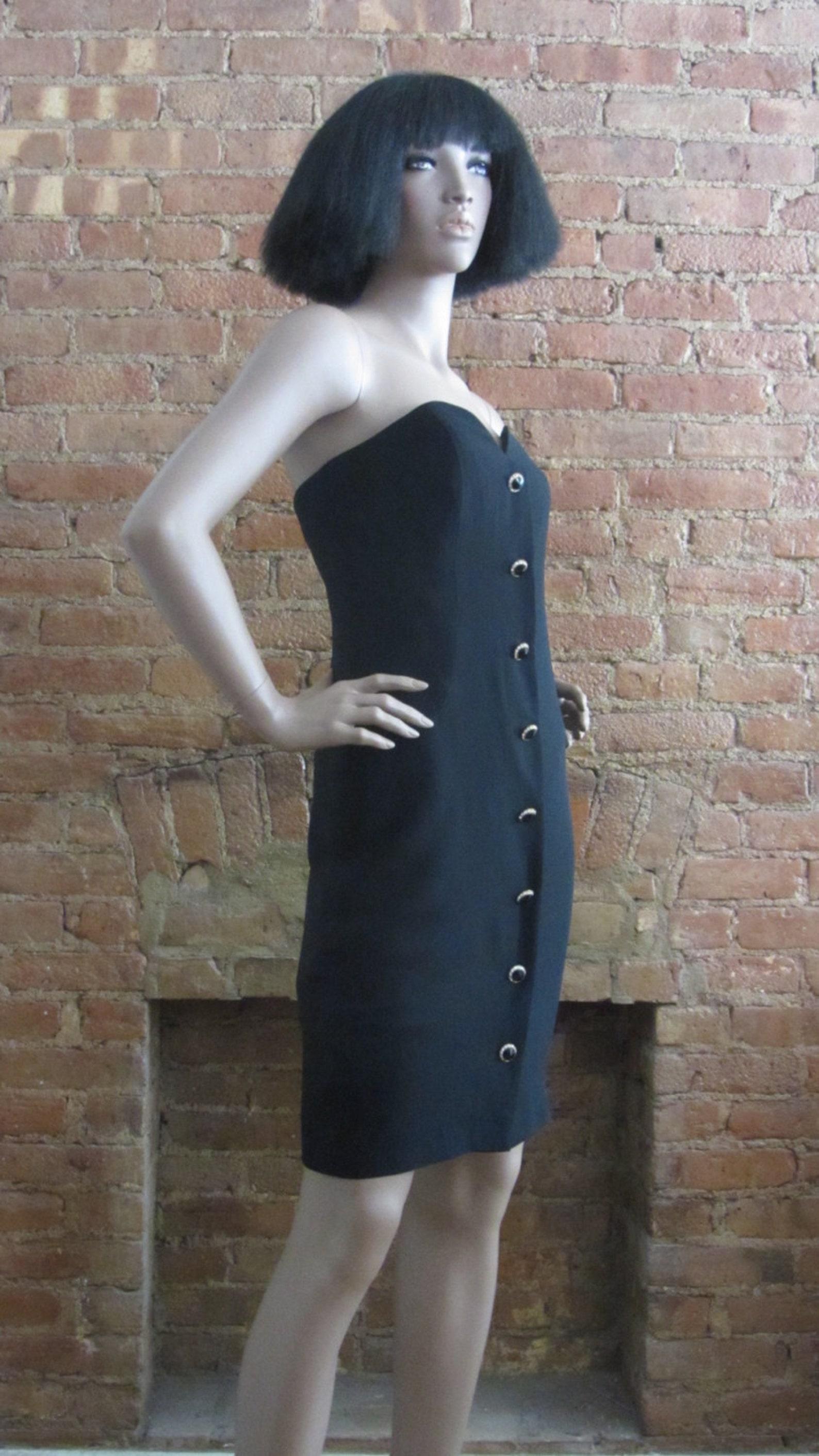 Vintage black crepe cocktail dress. straight silhouette. strapless boned sweetheart bodice. gorgeous faux onyx, gold & rhinestone buttons. back zip closure. dress is lined.

Circa: Early 1990s
Label: A.J. Bari
Color: Black
Fabric: Acetate,