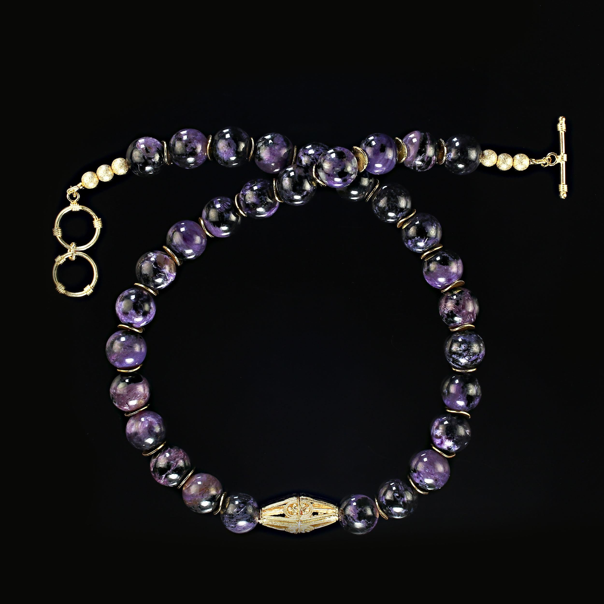 22 Inch glowing charoite in large 14 mm beads with an elegant gold tone focal and gold tone flutters accents the purple charoite beads.  The black matrix mixed with the purple enhances each unique bead.  This necklace is secured with a gold plated 2