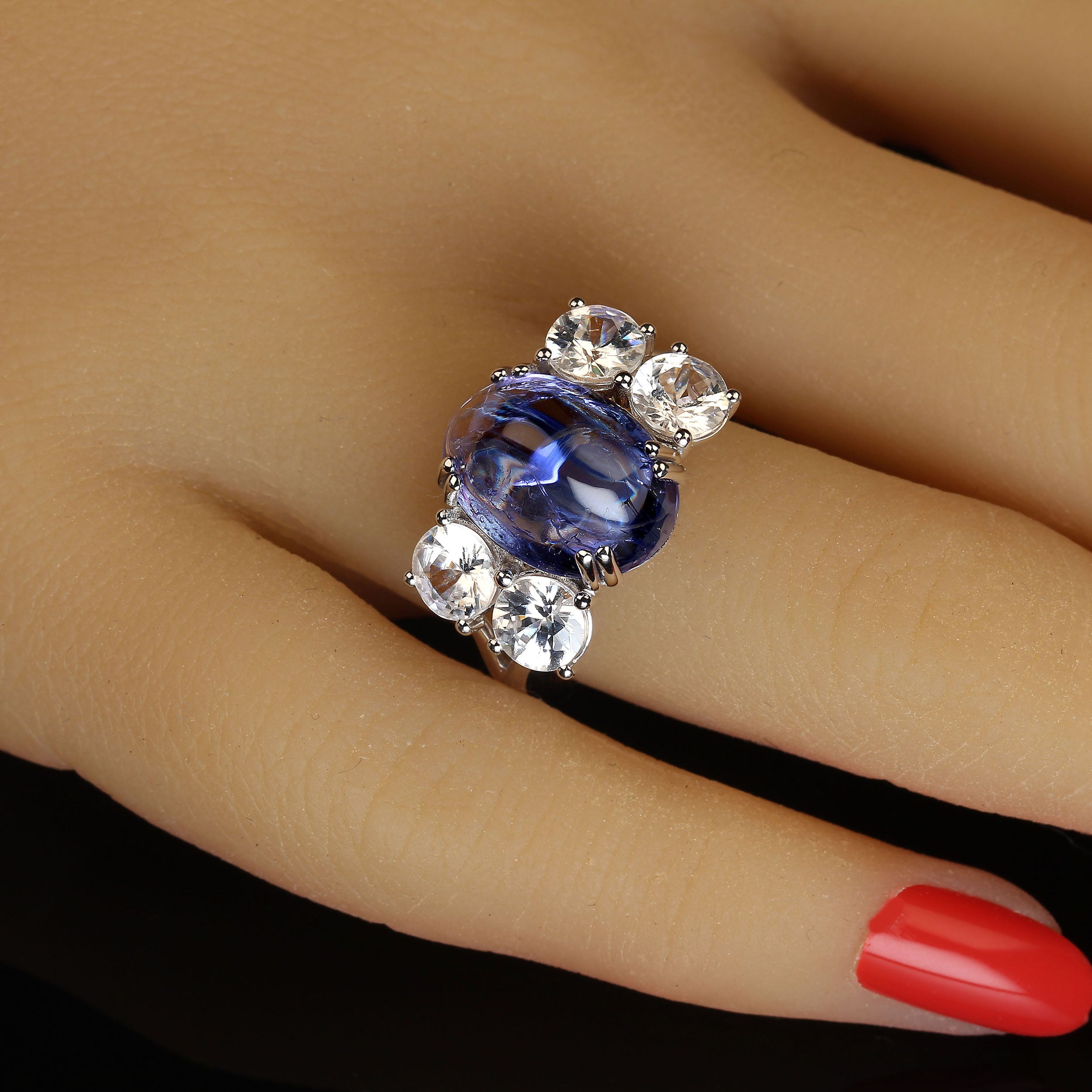 Wunderschönes Abendessen mit einem sauberen, blau-violett funkelnden ovalen Tansanit-Cabochon, der von zwei Paaren glitzernder farbloser echter Zirkone ergänzt wird.  Dieser atemberaubende, blinkende Ring wird Sie überall begeistern. Die