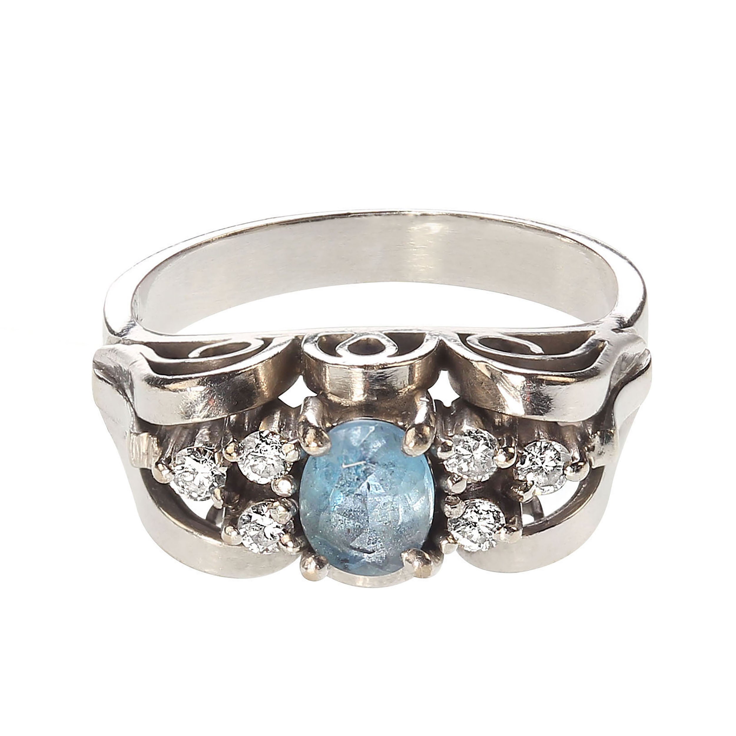 This beautiful ring was created in Brazil with a gorgeous local aquamarine.  The intensely blue, 5x3mm, aquamarine is accented with three diamonds on each side.  The lovely scrolly work in 18K white gold sets the gemstones up from the shank of the