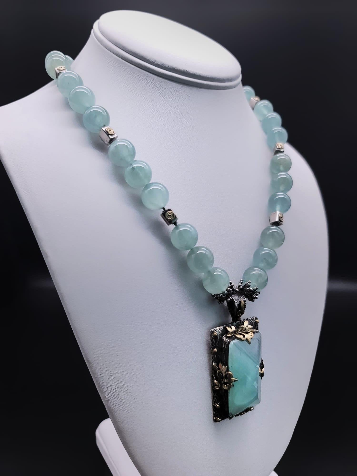 Discover the unparalleled beauty of this one-of-a-kind necklace, where delicate pale green Aquamarine beads unite with the commanding presence of a handcrafted Bora pendant. At its core, a gracefully polished, pyramid-shaped Moss Green Aquamarine