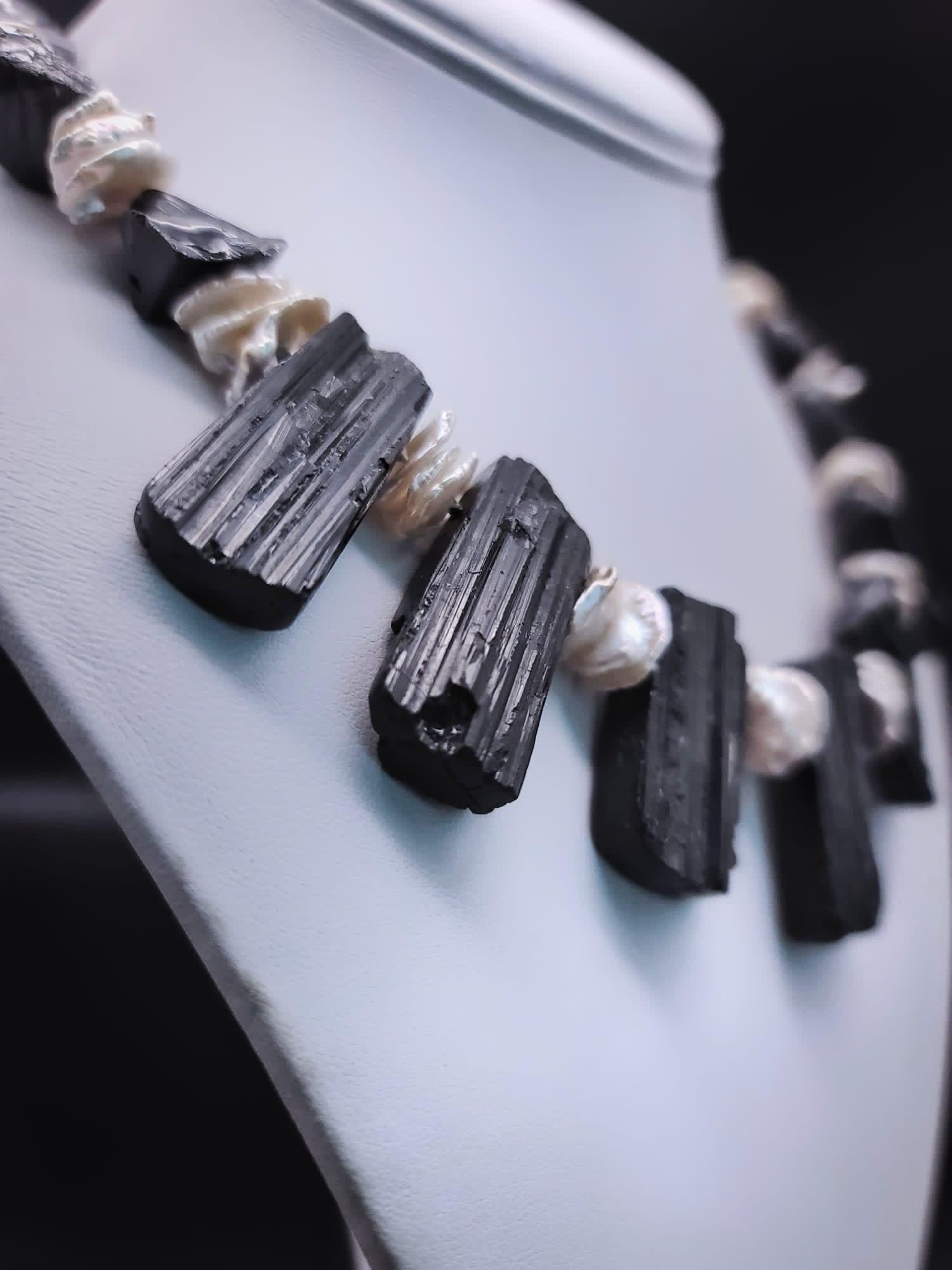One-of-a-Kind

Indulge in the allure of black and white with this exquisite Black Tourmaline and white pearl necklace. Large nuggets of rough-cut and polished Black Tourmaline are seamlessly mixed with center-drilled ruffled Keshi pearls, creating a