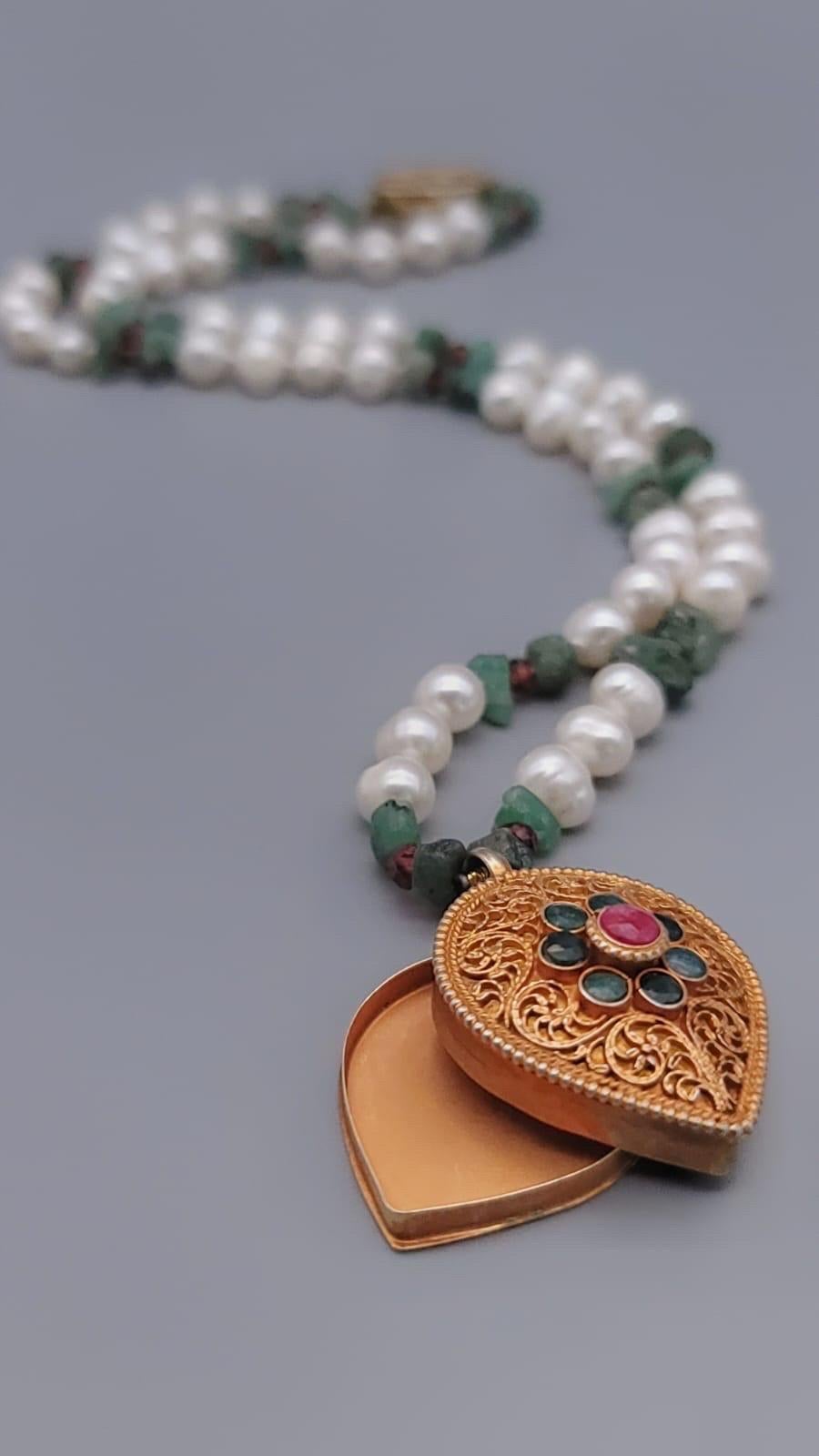 Unique en son genre

Boîte Ghau en forme de cœur incrustée d'émeraudes et de rubis, fabriquée à la main et suspendue à un collier de perles, rubis et émeraudes. 
Les boîtes à gau d'or au design traditionnel en filigrane, minutieusement fabriquées à