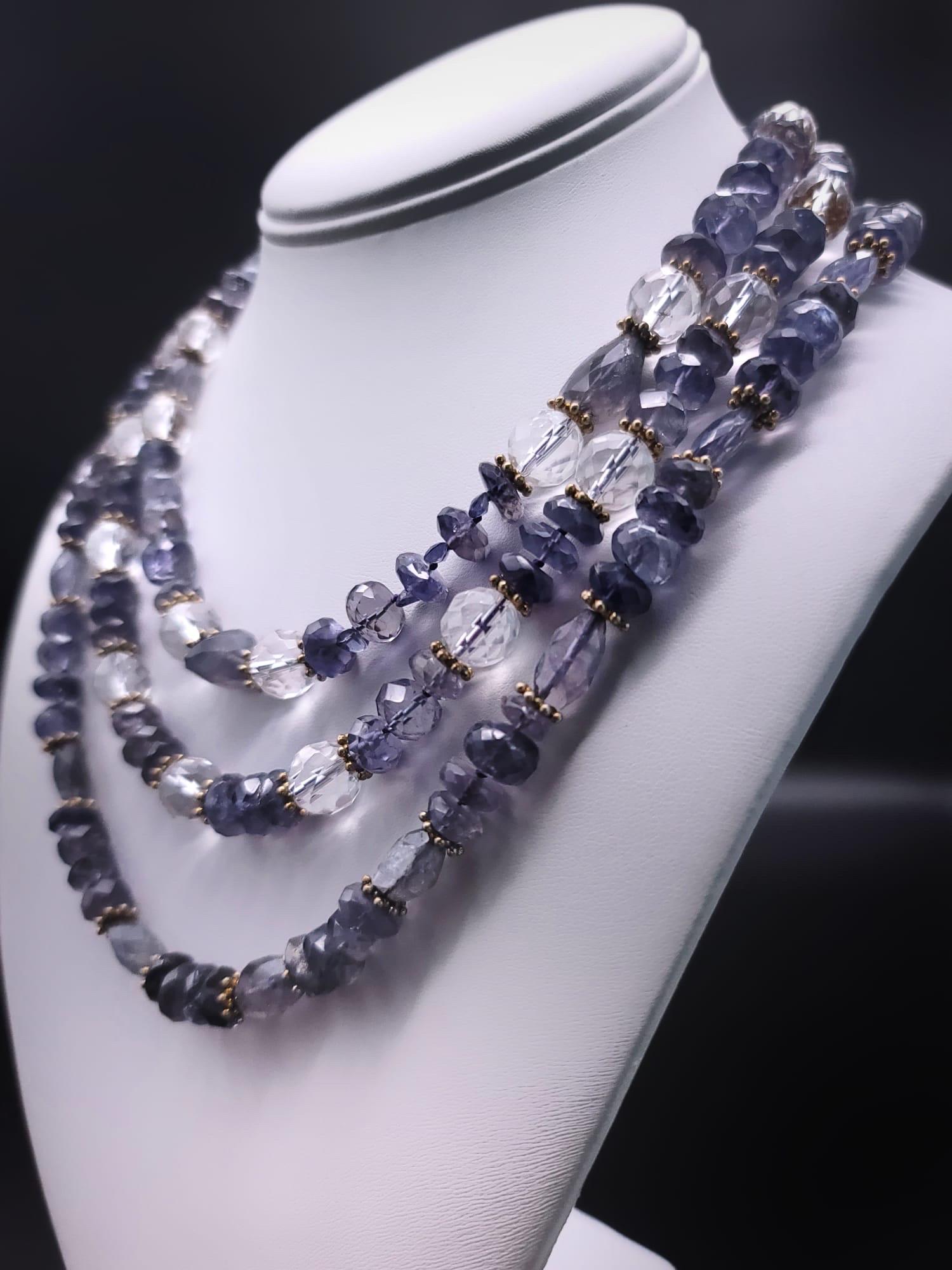 One-of-a-Kind
 
3-strand blue iolite and crystal faceted necklace. The stones are
Interspersed with vermeil rondels in 3 graduated strands. The strands are anchored by a 9 individual stone, ”Navaratna“ believed to bring well-being, good health, and